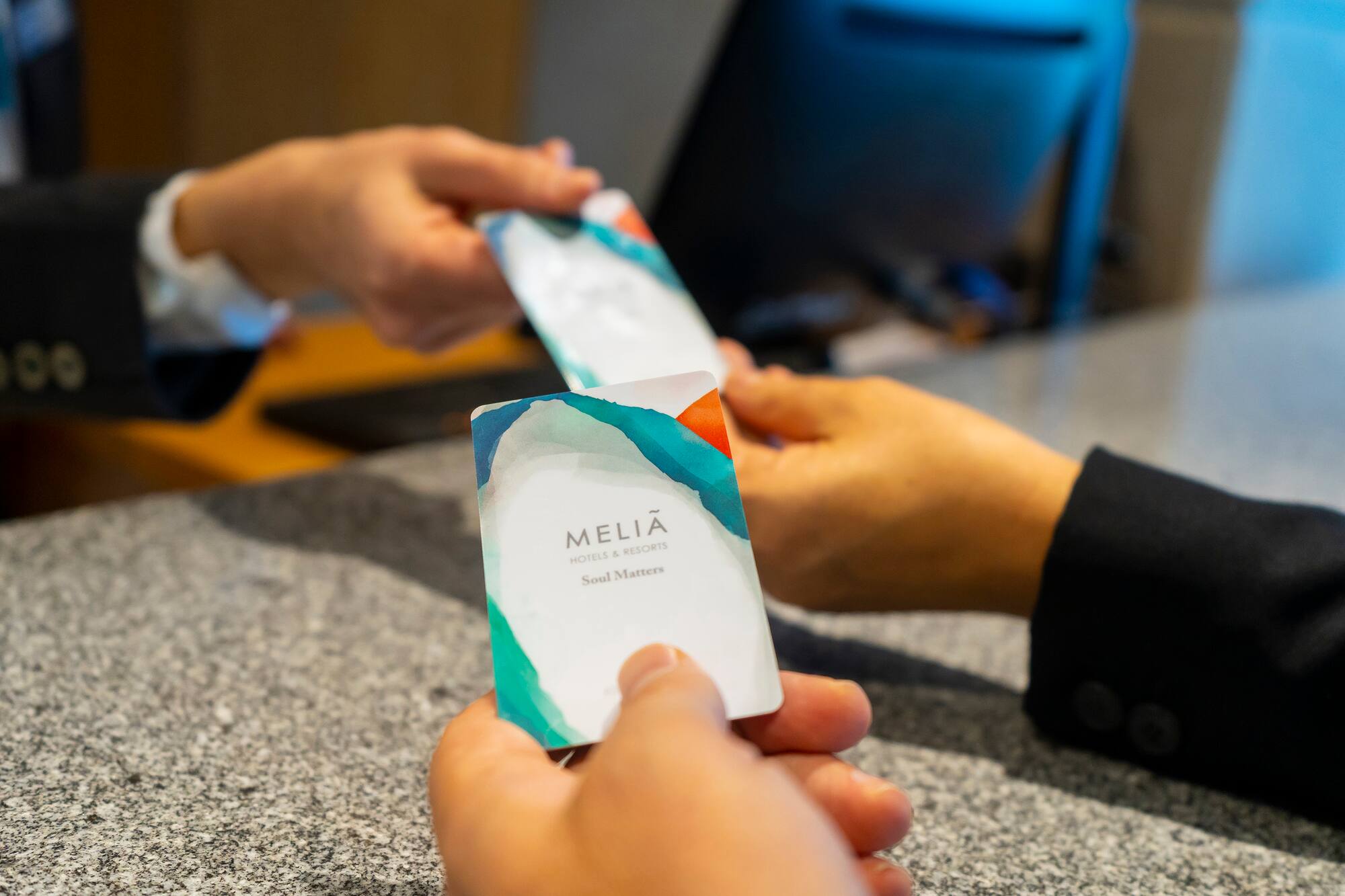 Close-up of hands exchanging Melia hotel key cards at reception.