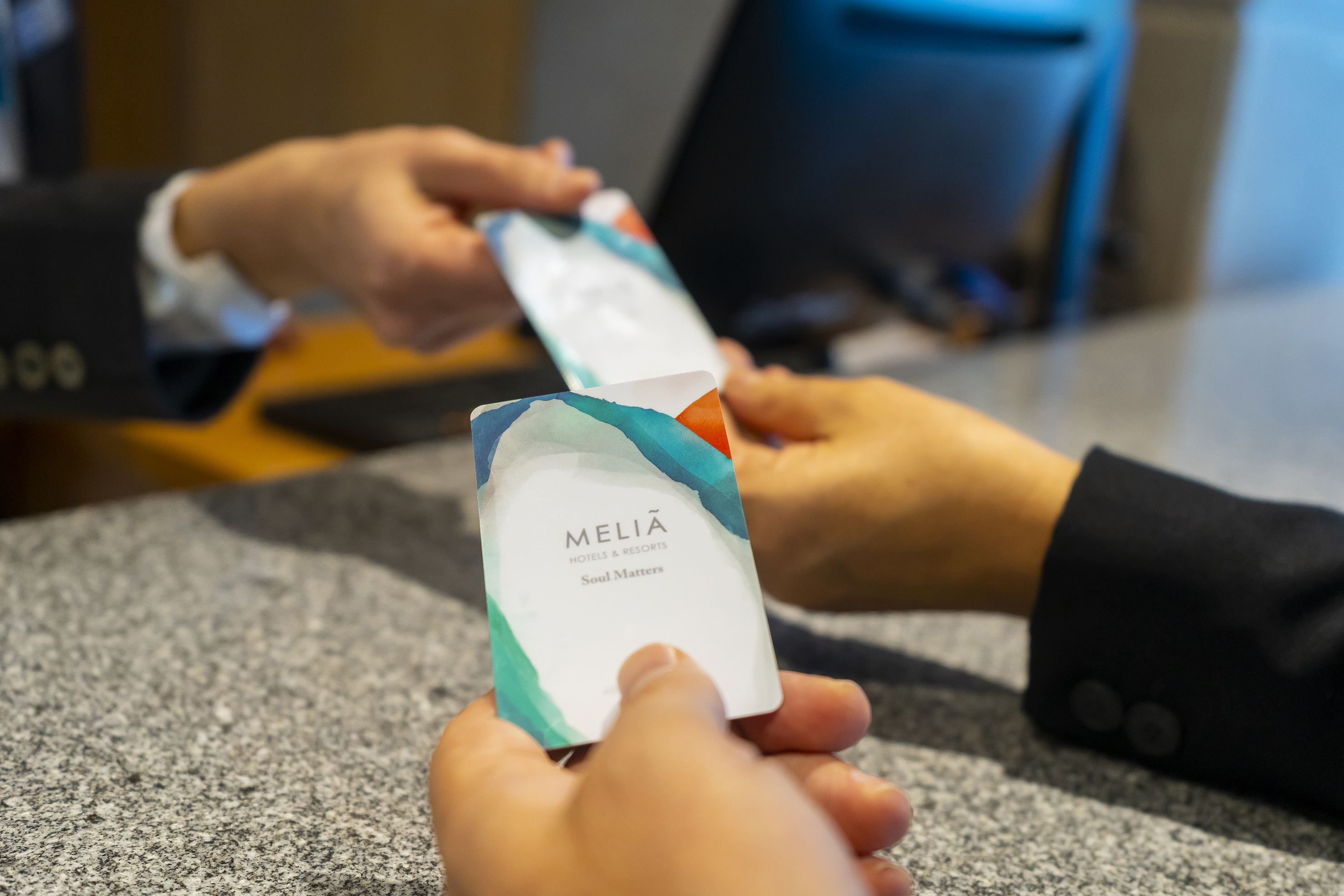 Close-up of hands exchanging Melia hotel key cards at reception.