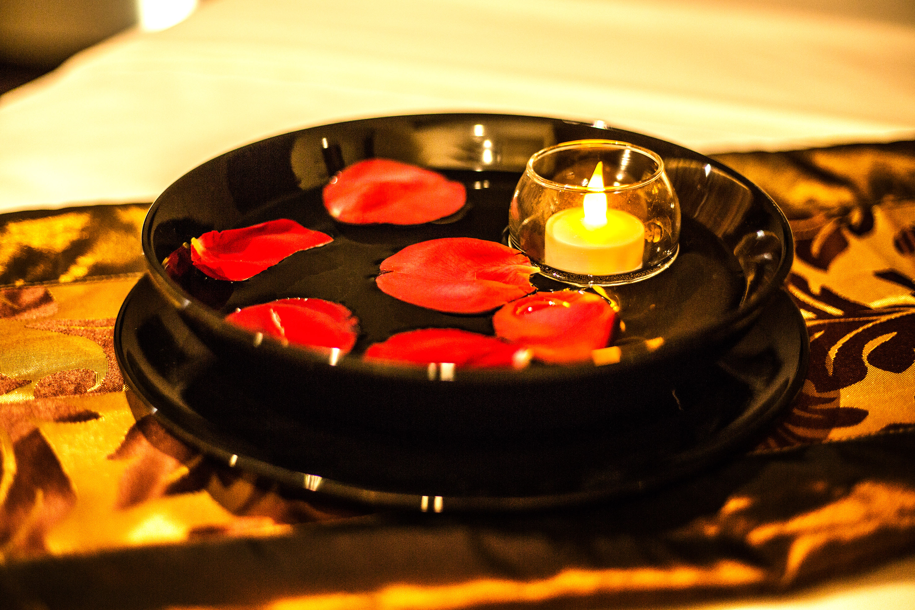 Floating candle, red rose petals in a black bowl for relaxing spa decor.