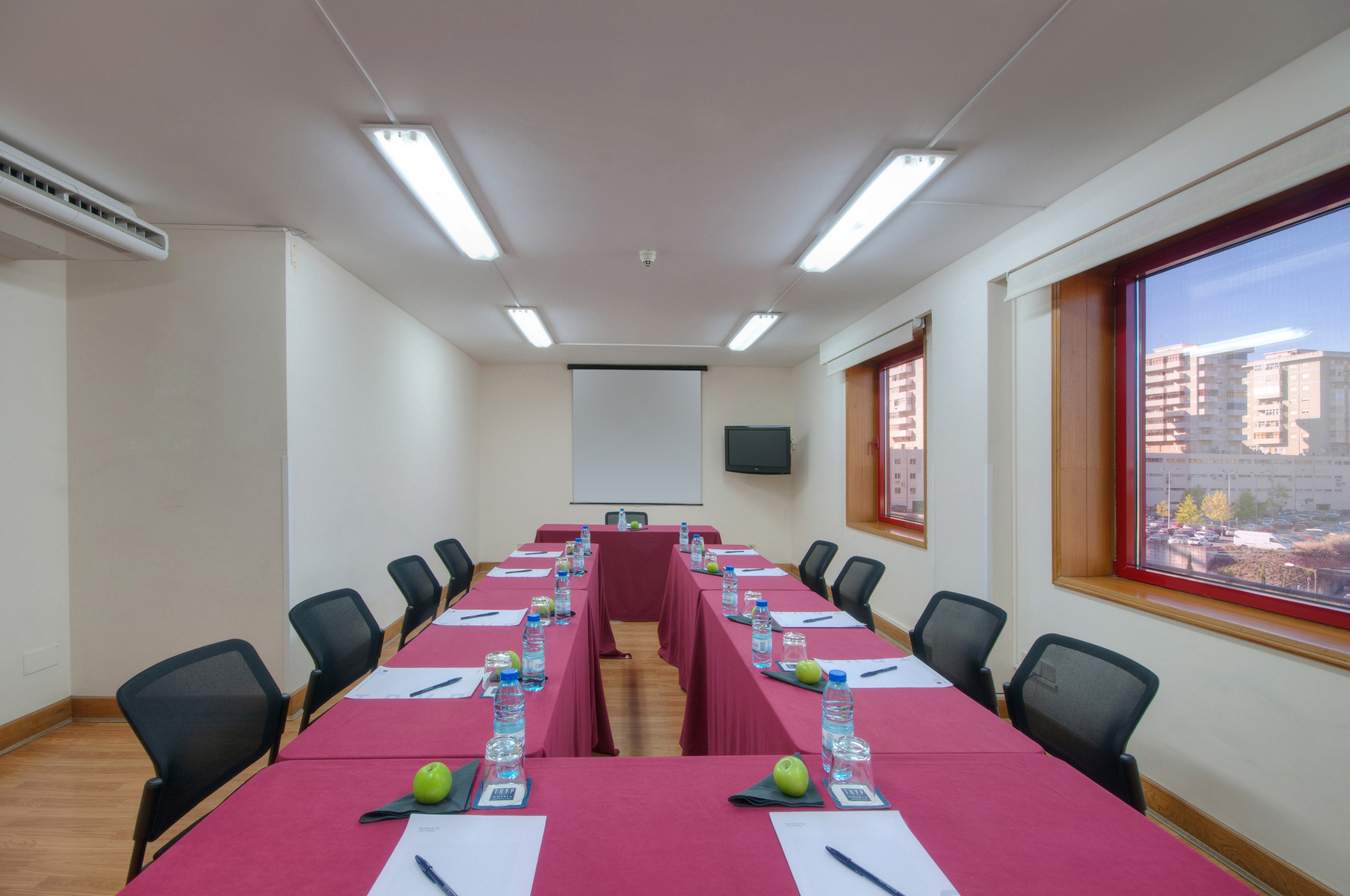 U-shaped conference room setup with projector, red tables, chairs, and city views.