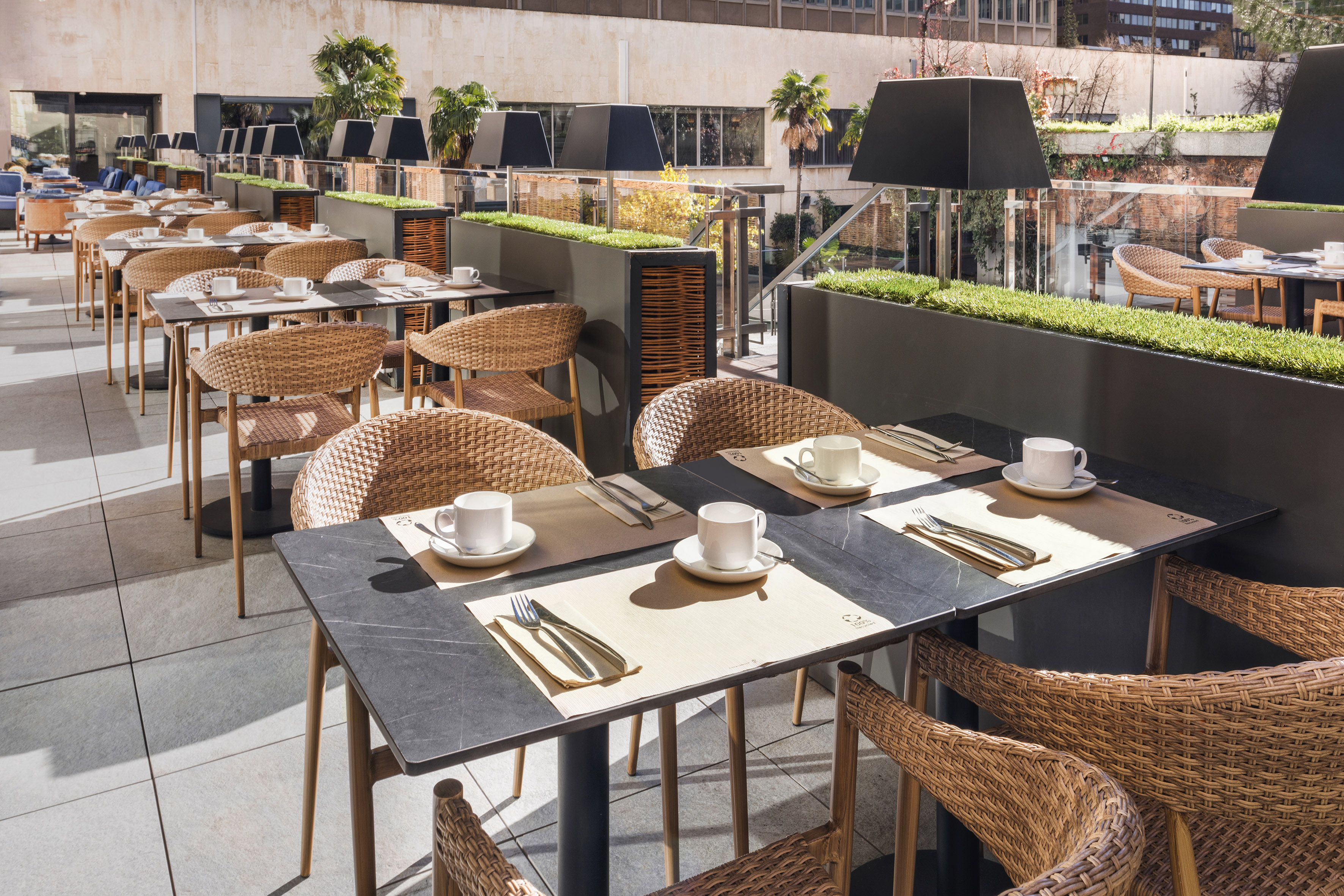Sunny outdoor restaurant terrace with many set tables and wicker chairs.