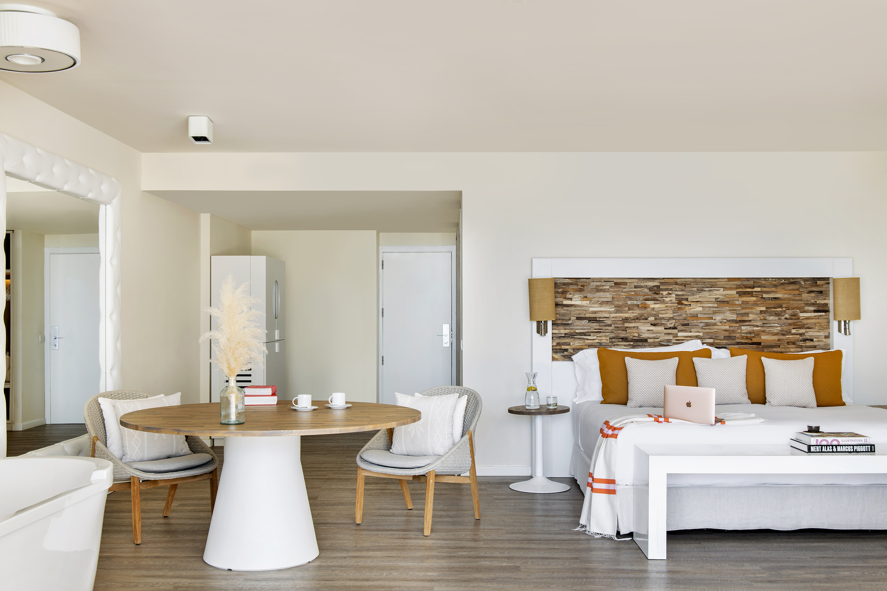 Modern hotel studio with bed, wooden headboard, dining table, and bathtub.