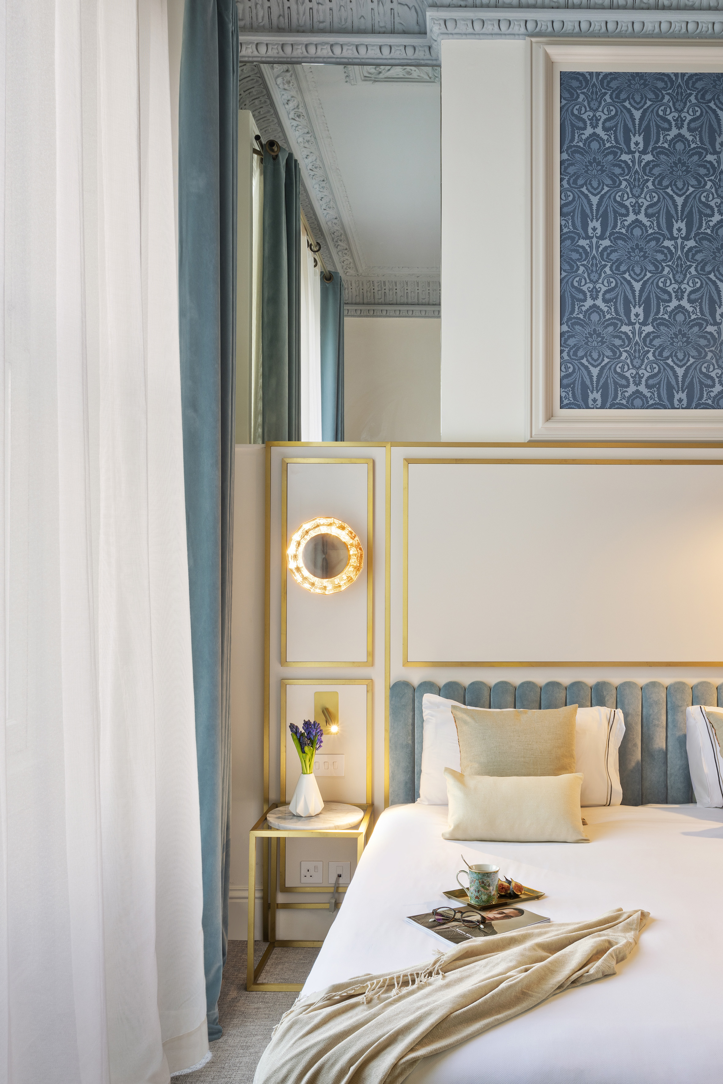 Luxury hotel bedroom with blue headboard, gold trim, and elegant decor.