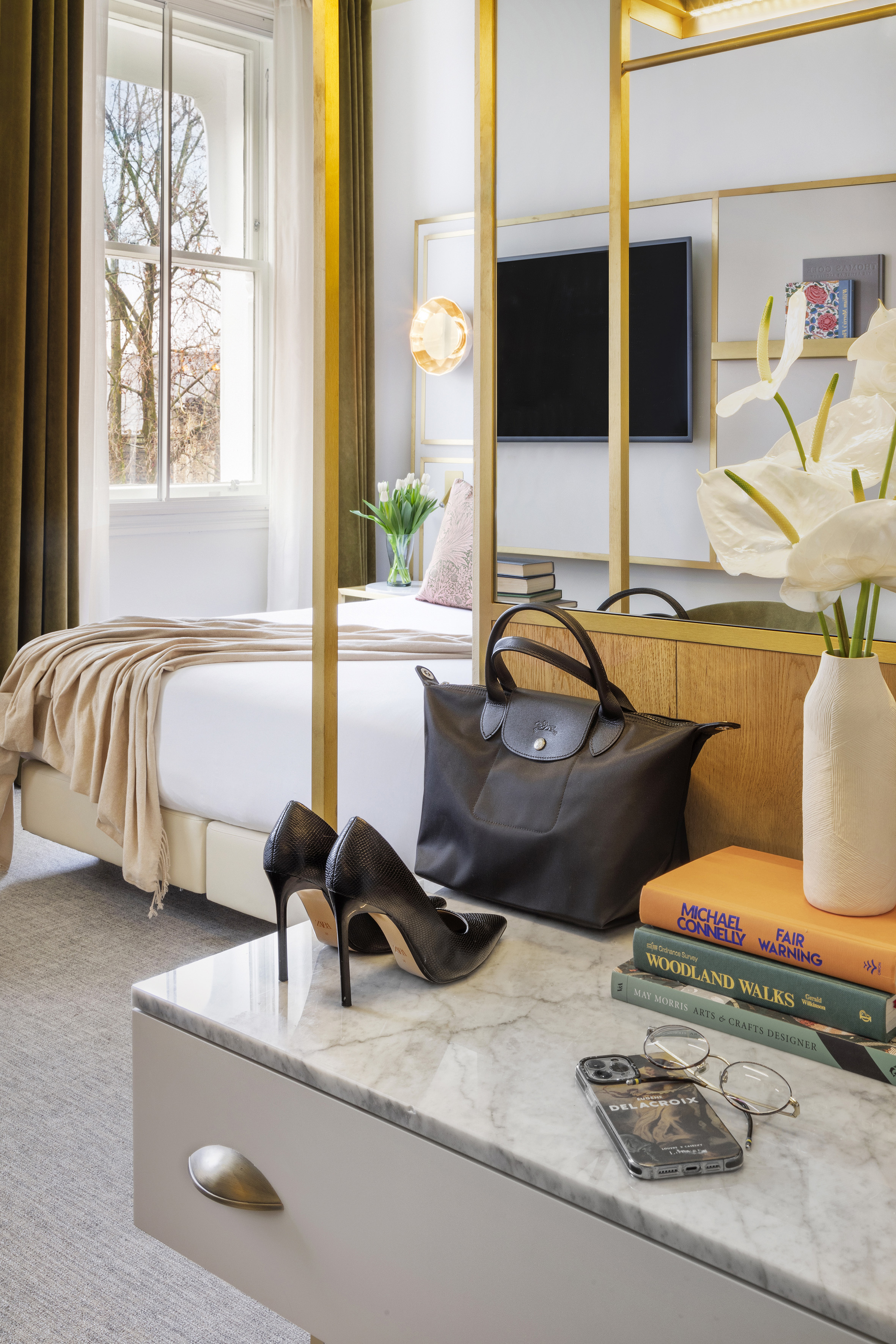 Modern hotel bedroom with gold divider, marble vanity, black heels, tote bag, and books.
