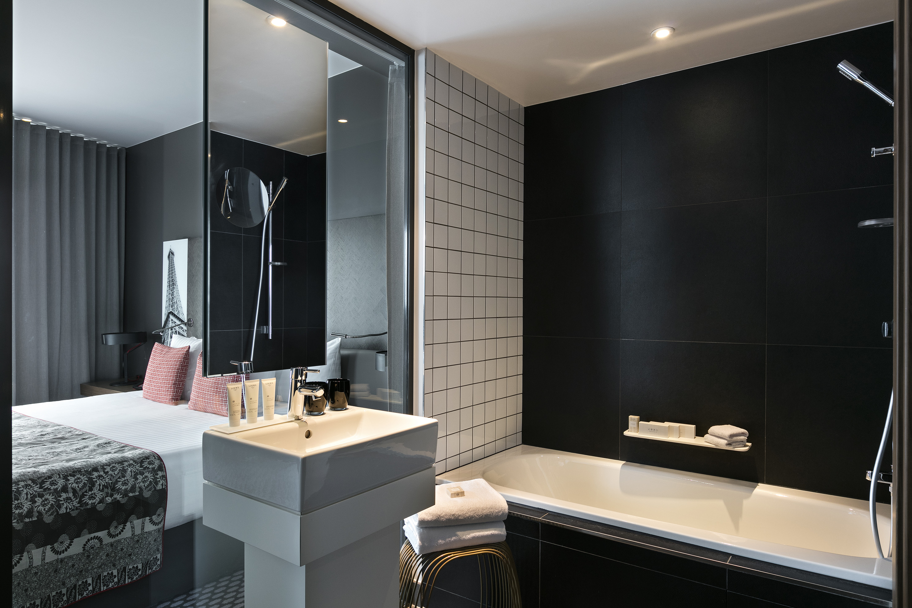 Modern hotel room: black & white bathroom, white tub, sink, and bed.
