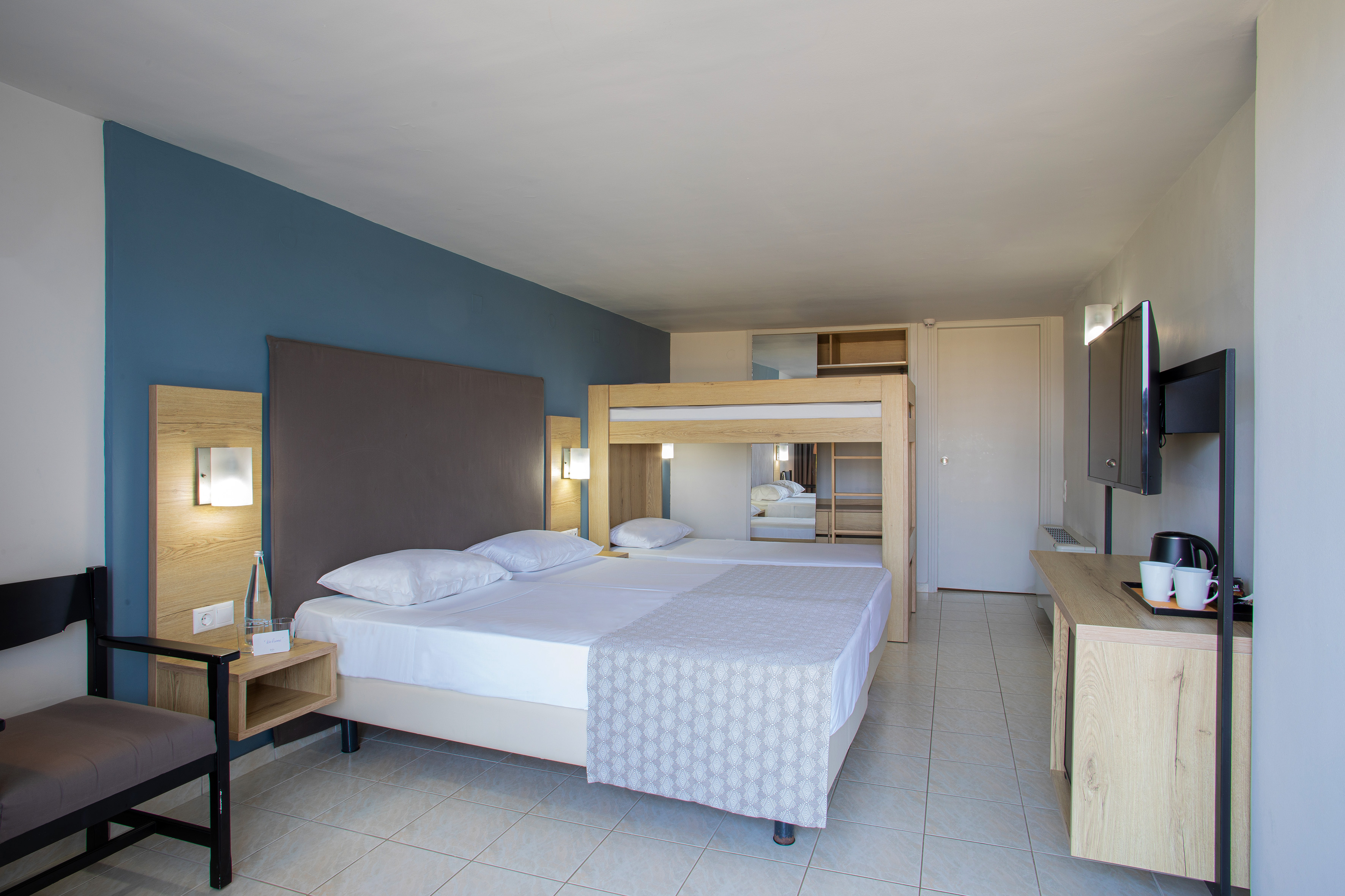 Hotel family room with twin beds, bunk bed, TV, and modern wood decor.