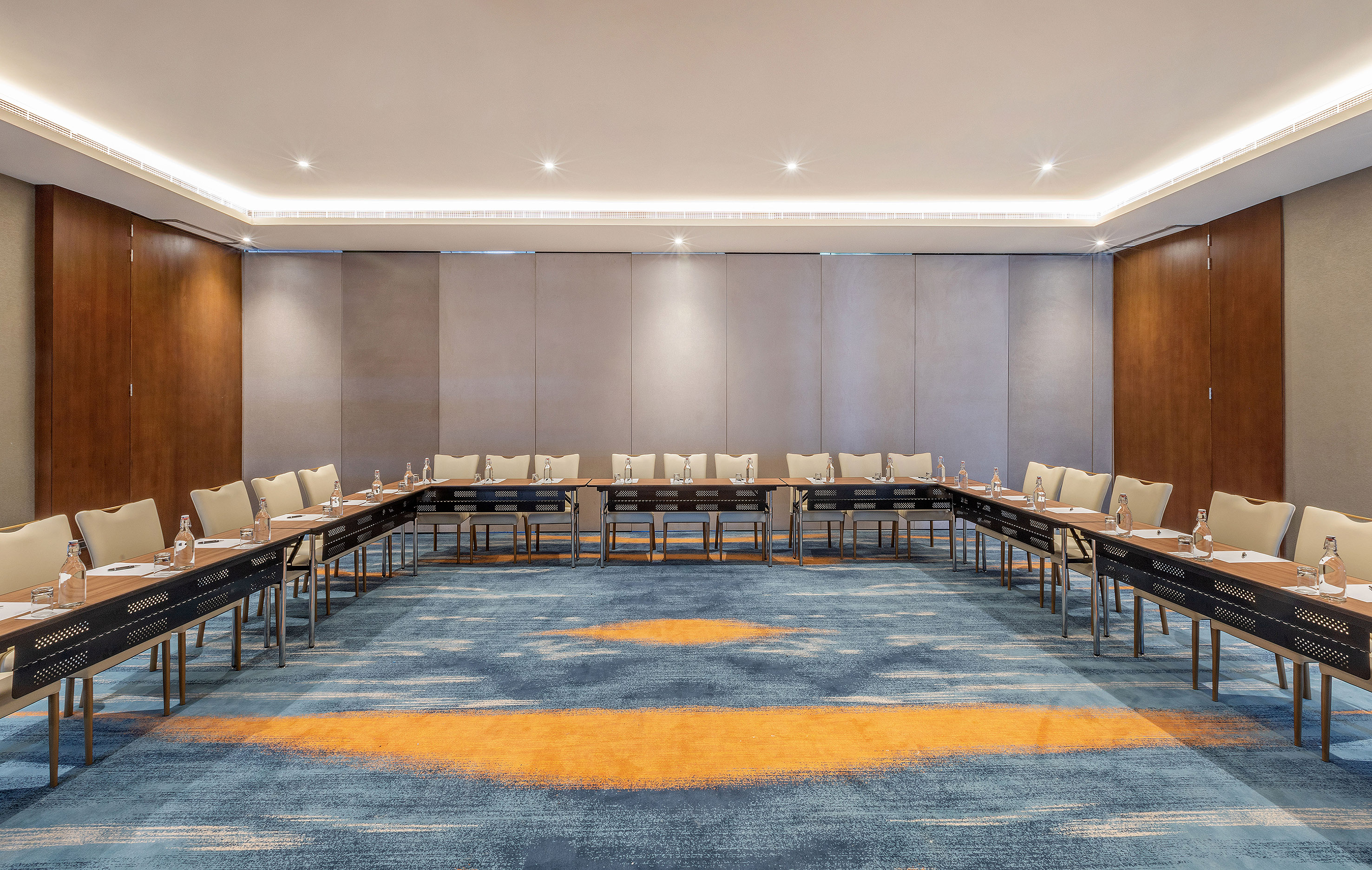 U-shape conference room setup with modern tables, chairs, and patterned blue carpet.