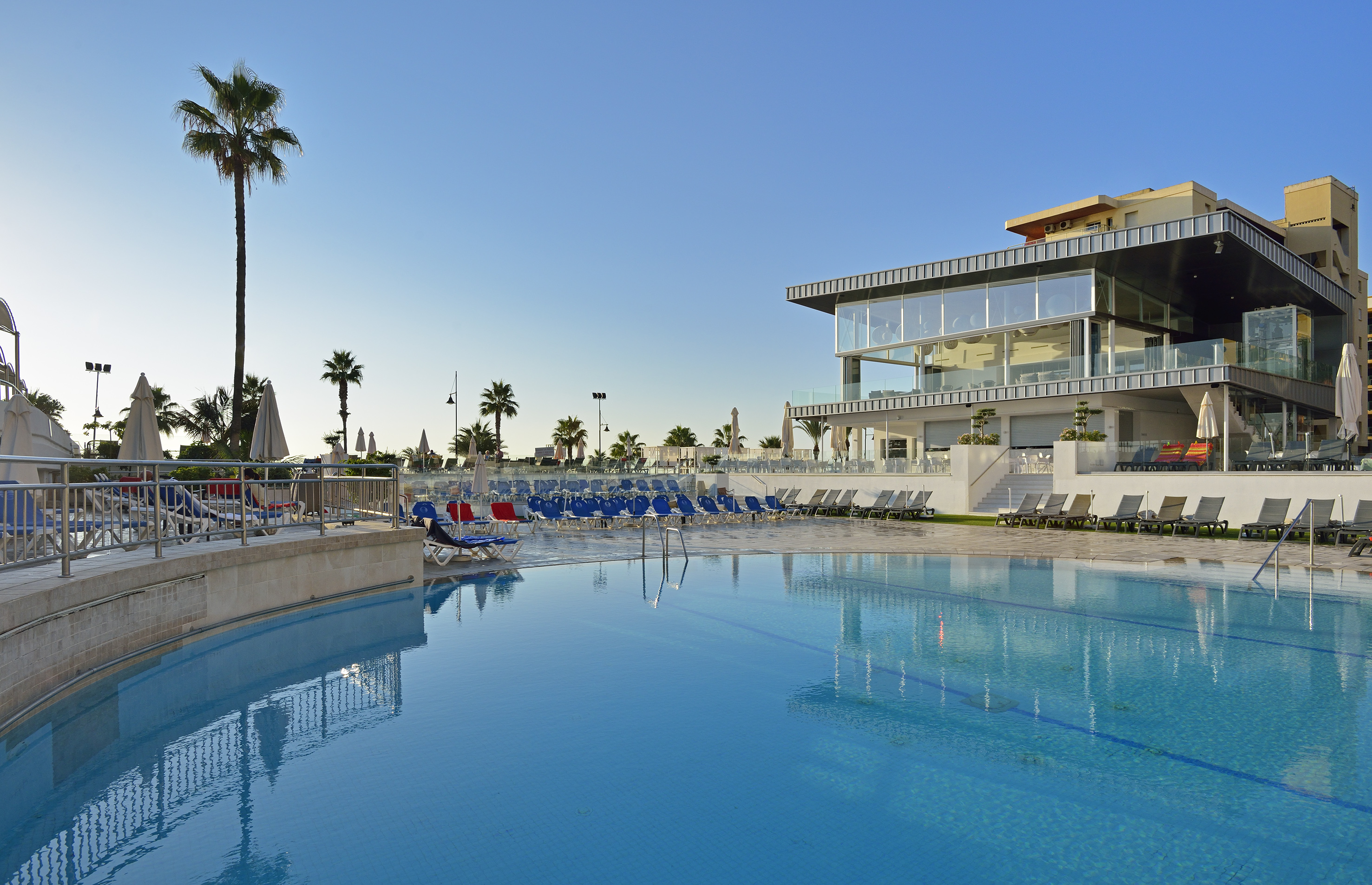 Modern resort hotel pool with palm trees & sun loungers.