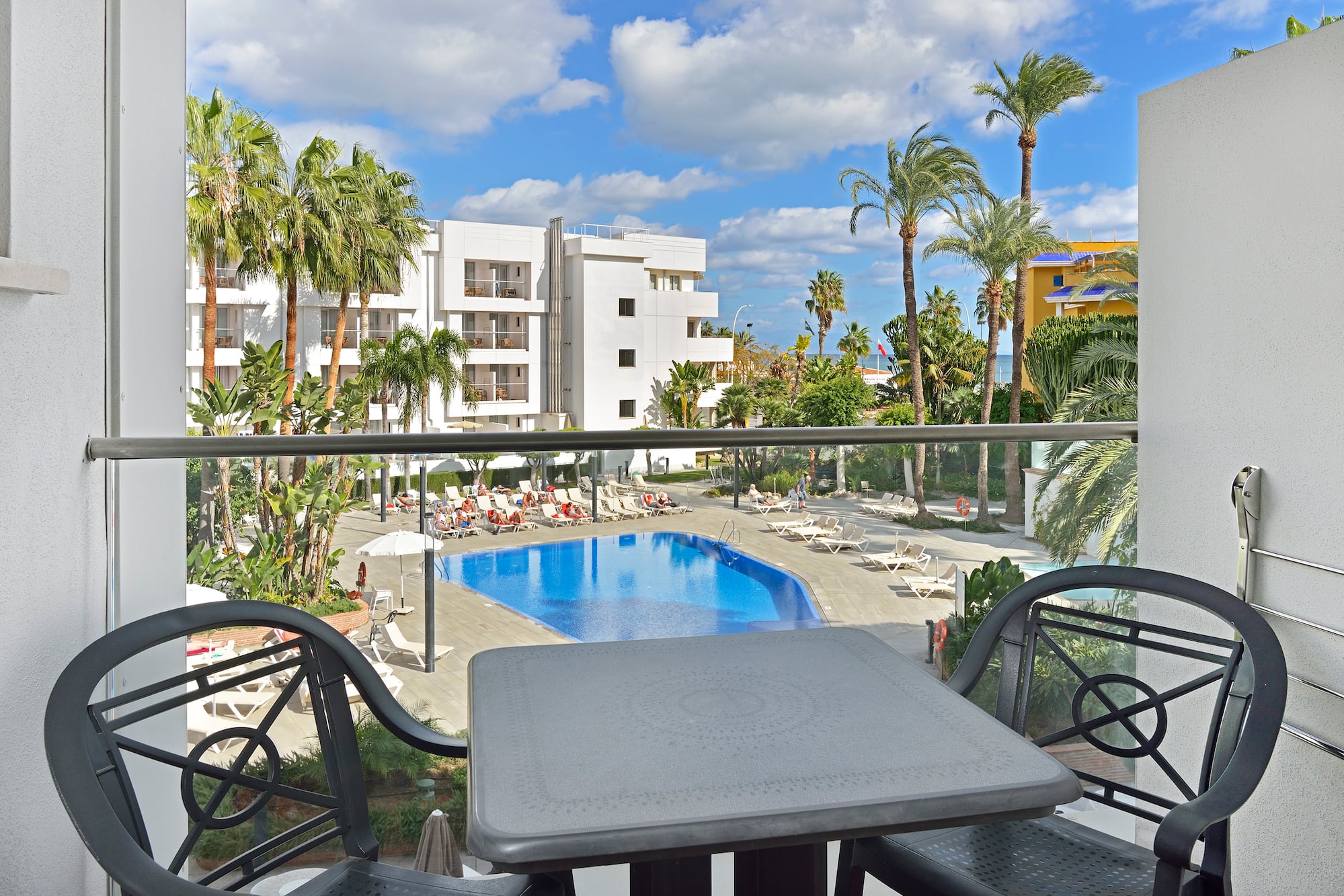 Resort hotel balcony view: swimming pool, sun loungers, and palm trees.