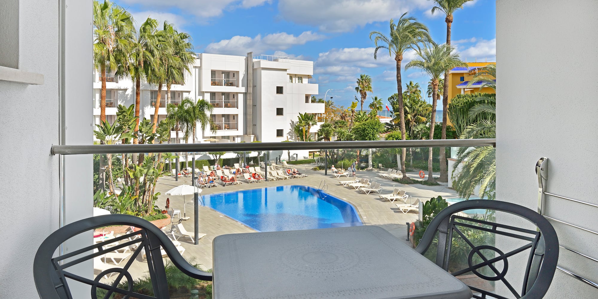 Resort hotel balcony view: swimming pool, sun loungers, and palm trees.