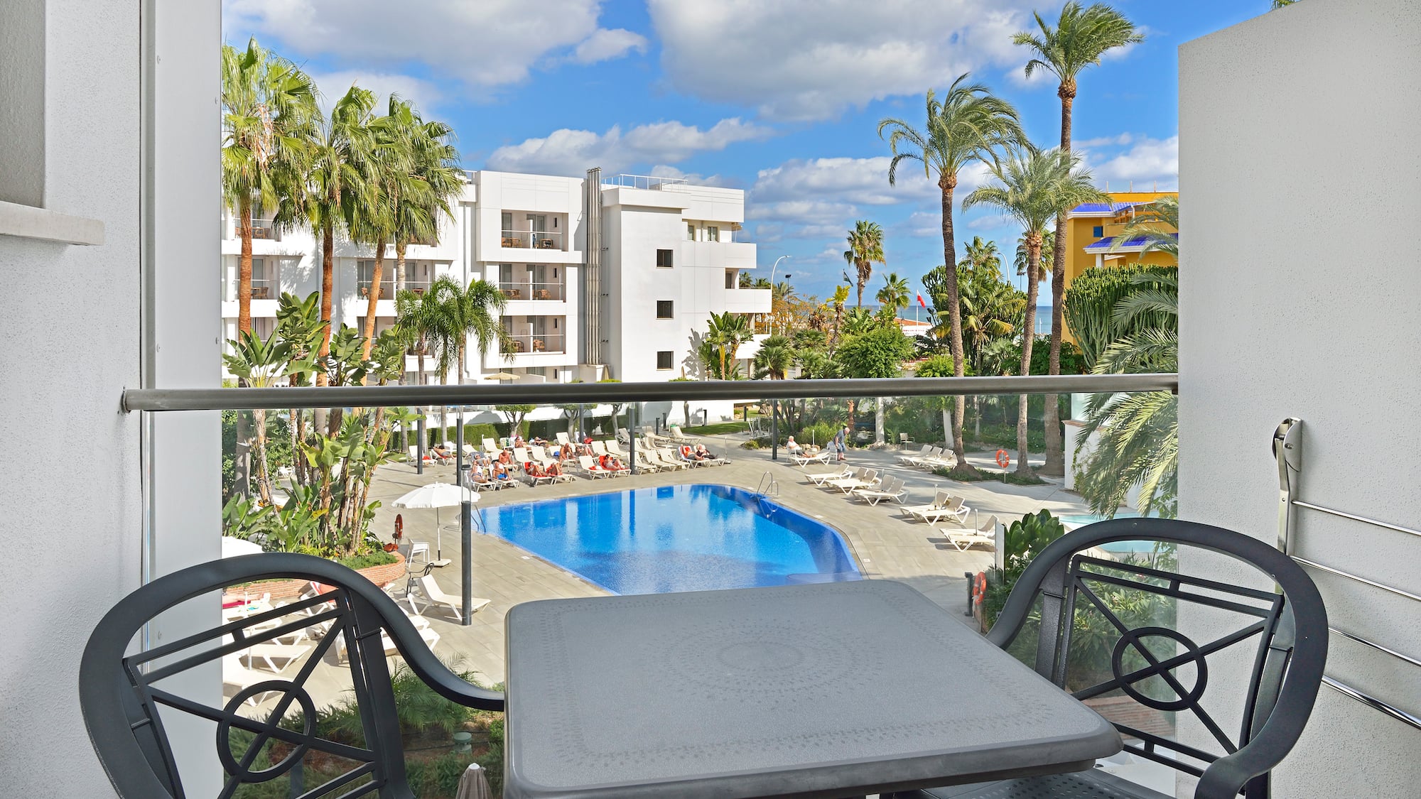 Resort hotel balcony view: swimming pool, sun loungers, and palm trees.