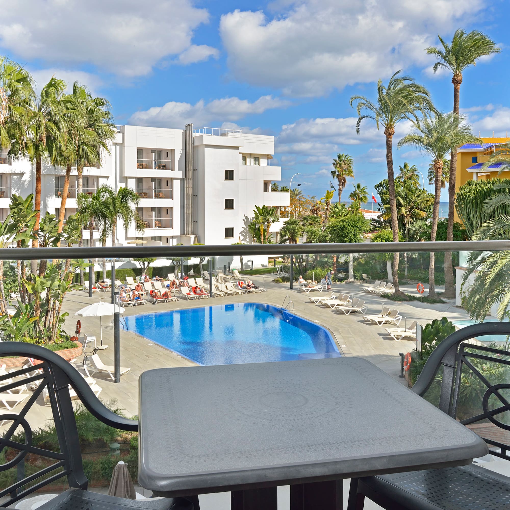 Resort hotel balcony view: swimming pool, sun loungers, and palm trees.