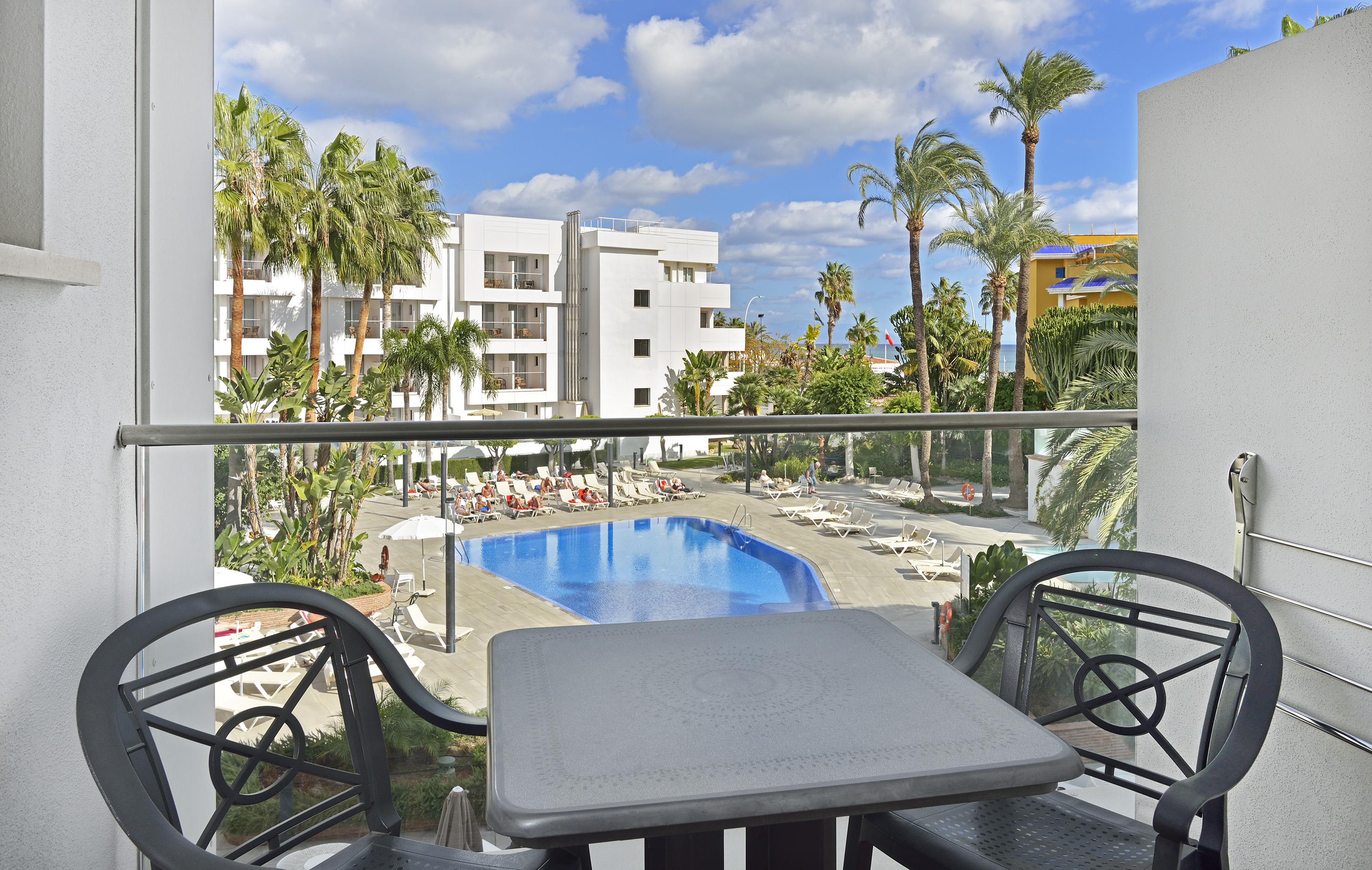 Resort hotel balcony view: swimming pool, sun loungers, and palm trees.