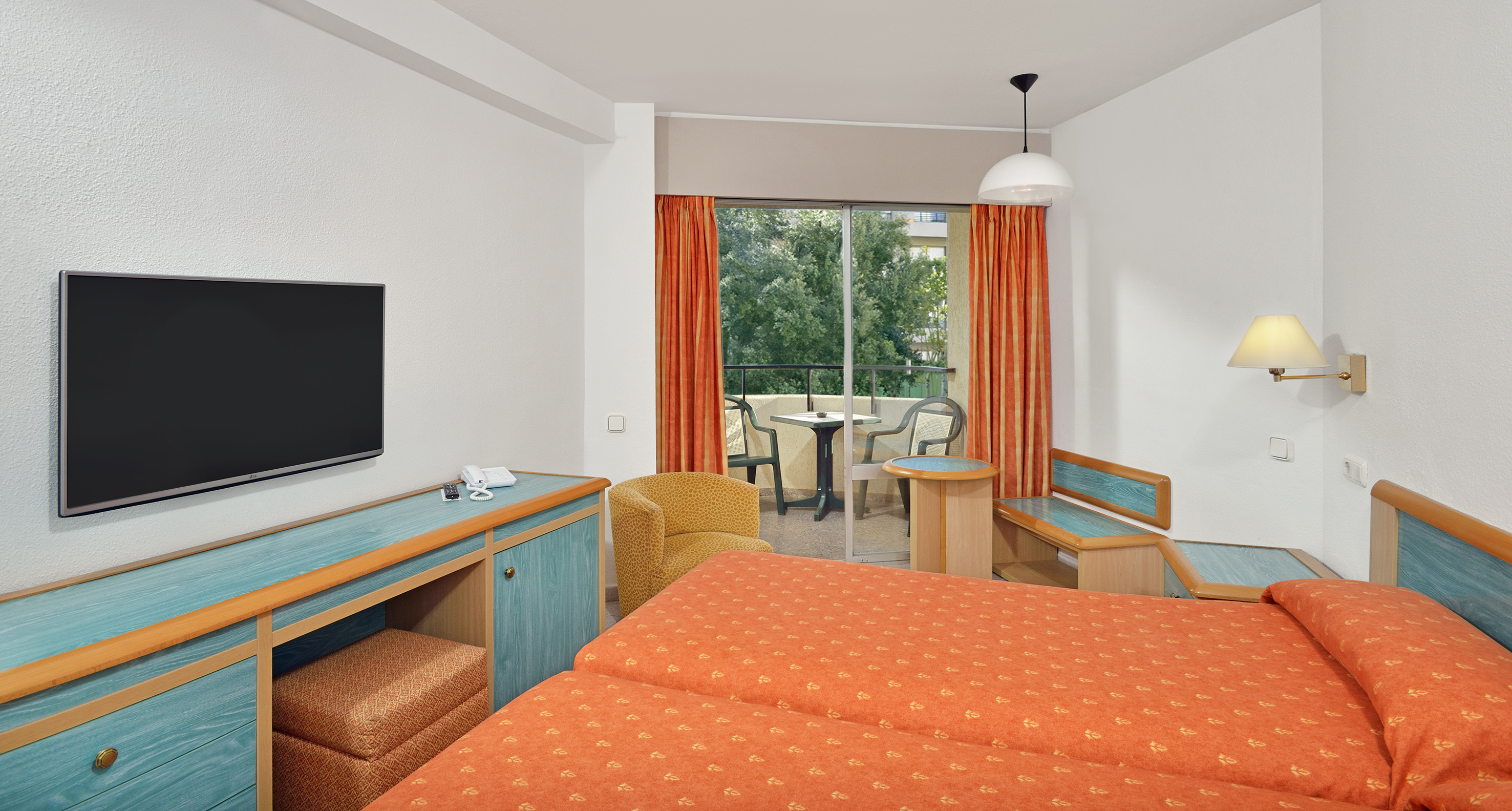 Hotel room with twin beds, balcony, flat-screen TV, and orange decor.