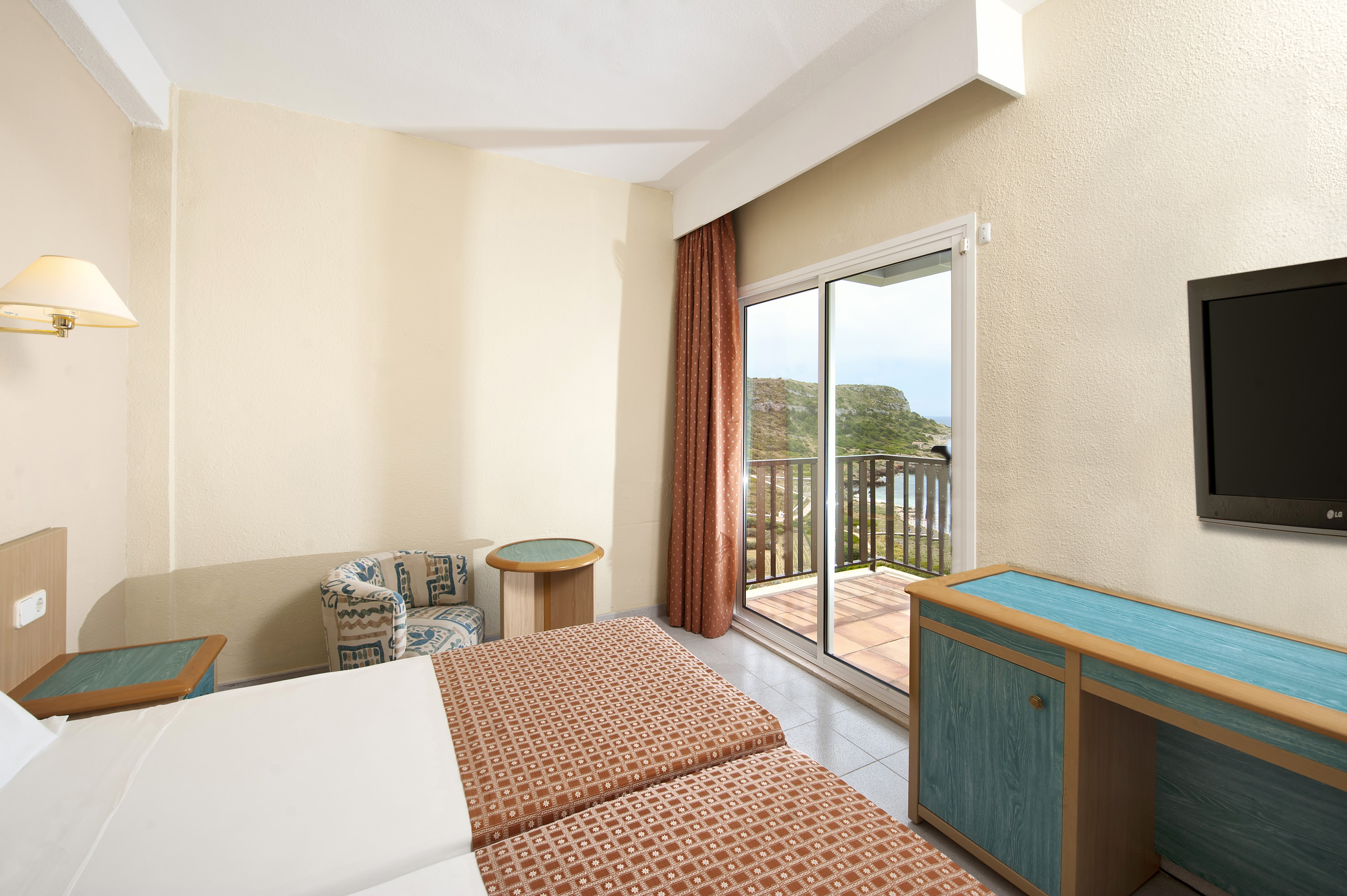 Hotel bedroom with twin beds, balcony, cliffside sea view, and wall-mounted TV.