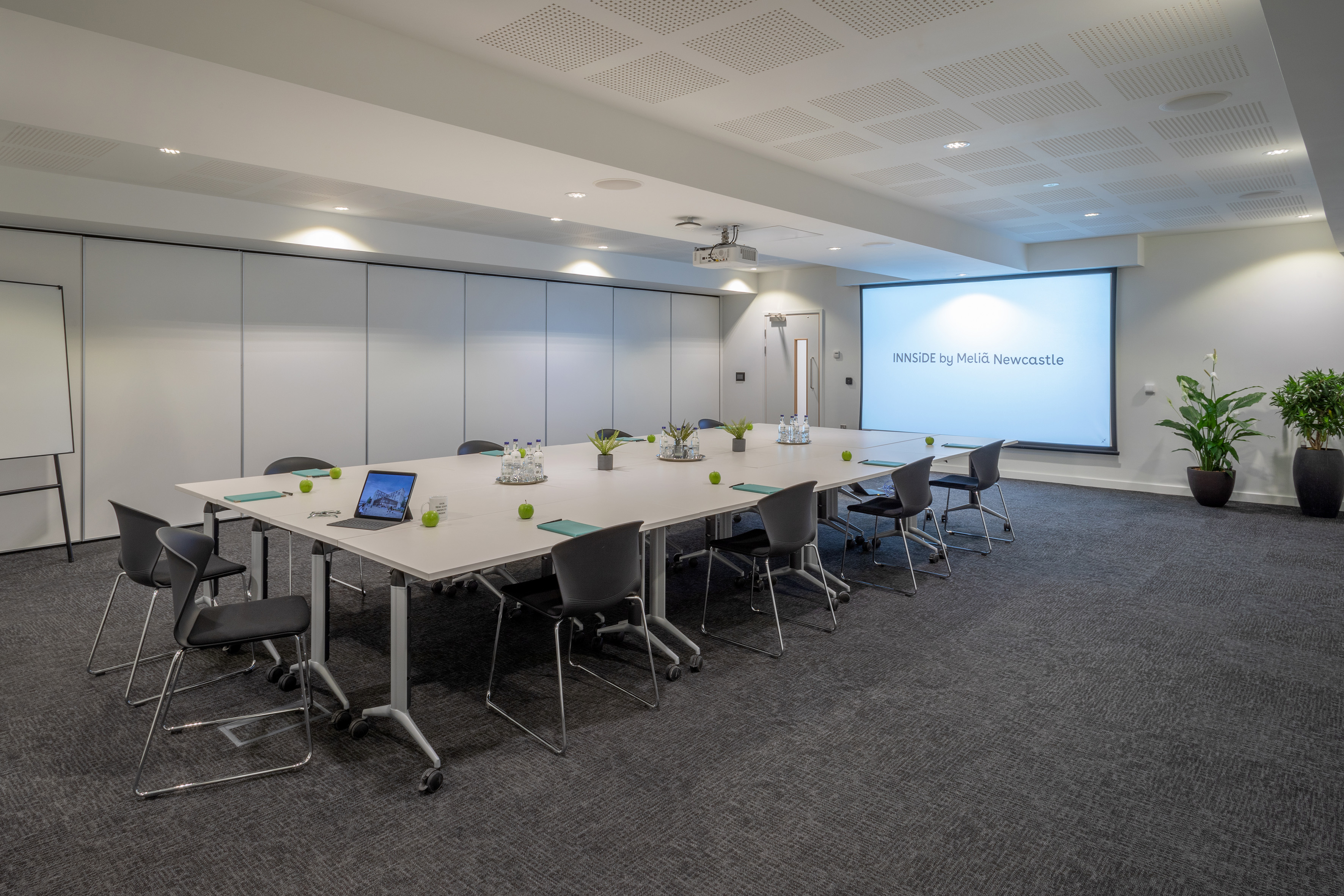 Modern meeting room at INNSIDE Newcastle with screen, long table, and chairs.
