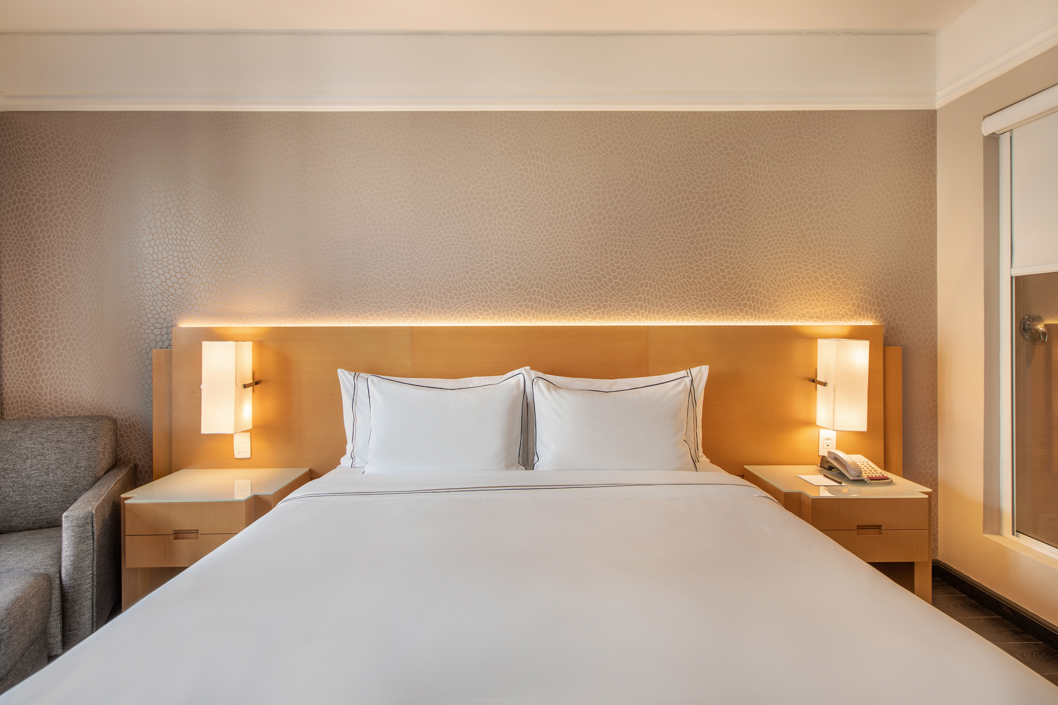 Hotel guest room with white bed, wood headboard, and lighted nightstands.