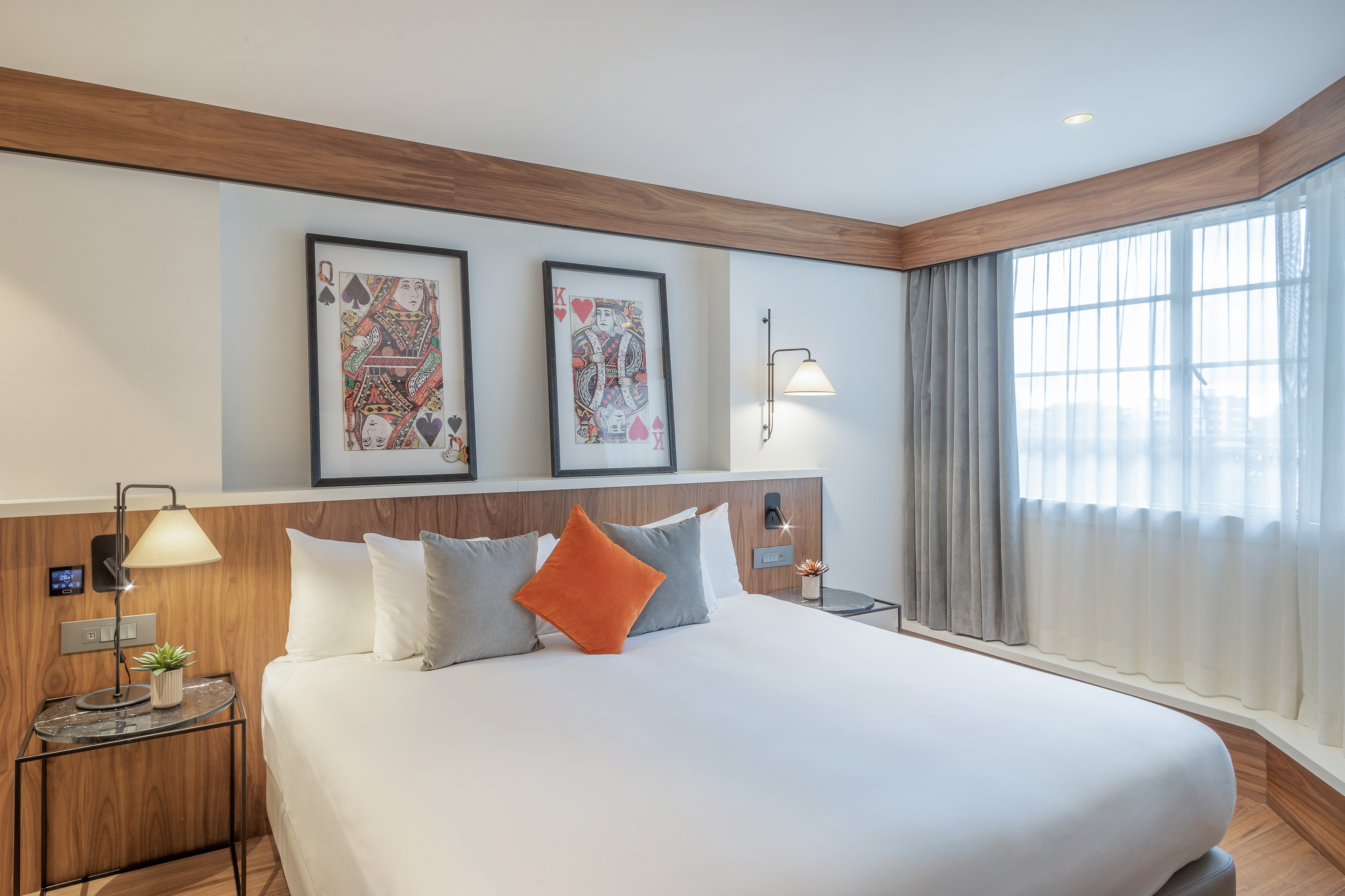 Modern hotel bedroom with queen bed, playing card art, wood details, and window.