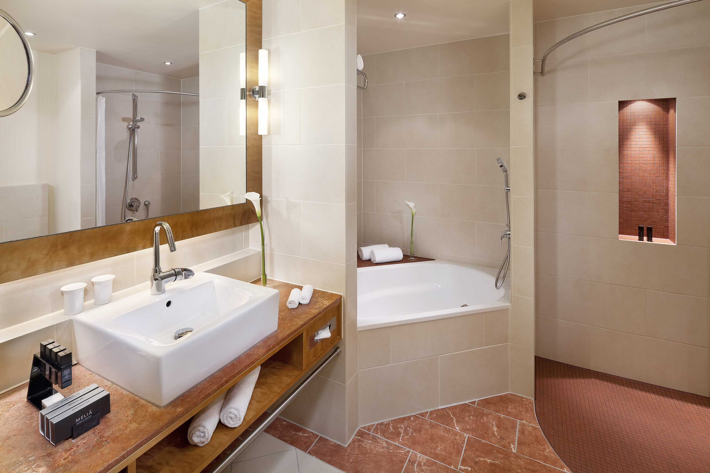 Modern hotel bathroom with white sink, marble vanity, bathtub, and shower.