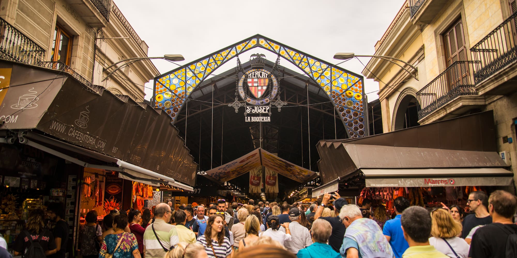 Entrada concurrida del Mercat La Boqueria en Barcelona, con arco de vidrieras.