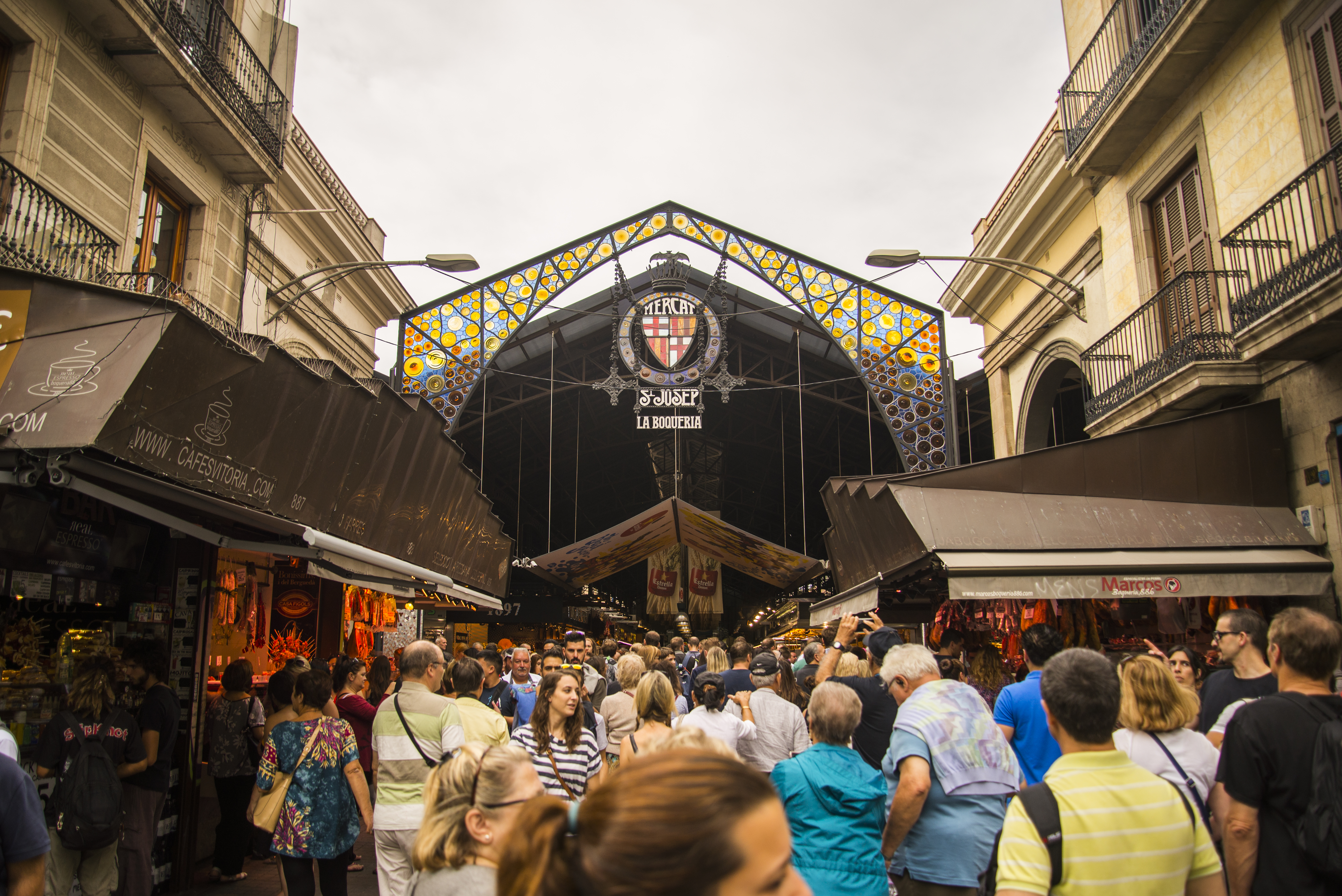 Entrada concurrida del Mercat La Boqueria en Barcelona, con arco de vidrieras.