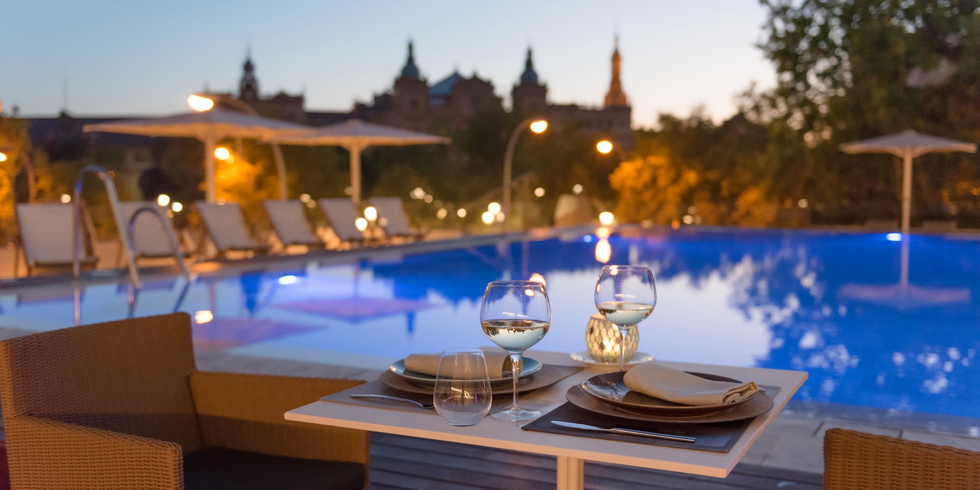 a table with wine glasses and plates on it by a pool