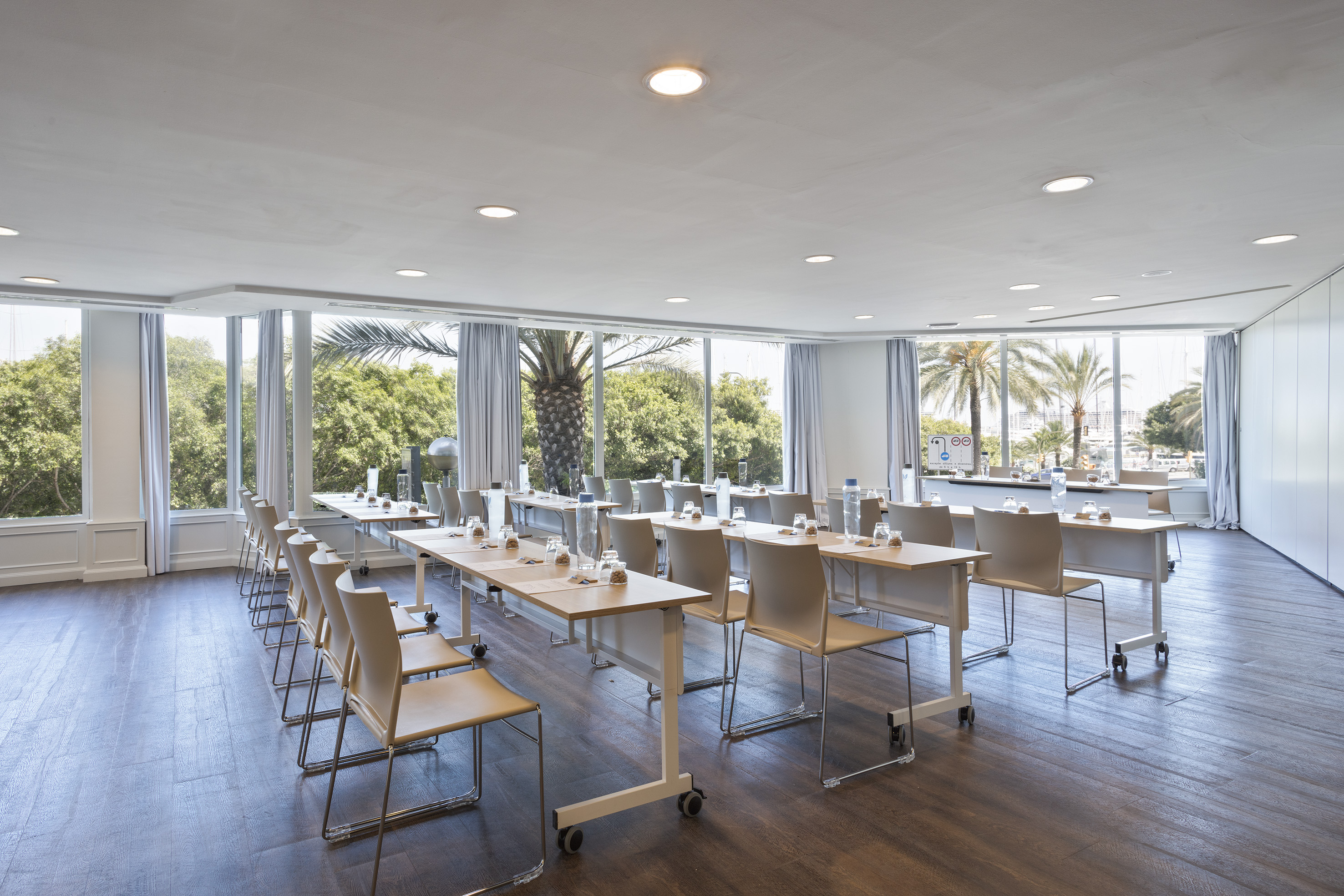Modern meeting room with classroom setup, large windows, and palm trees.