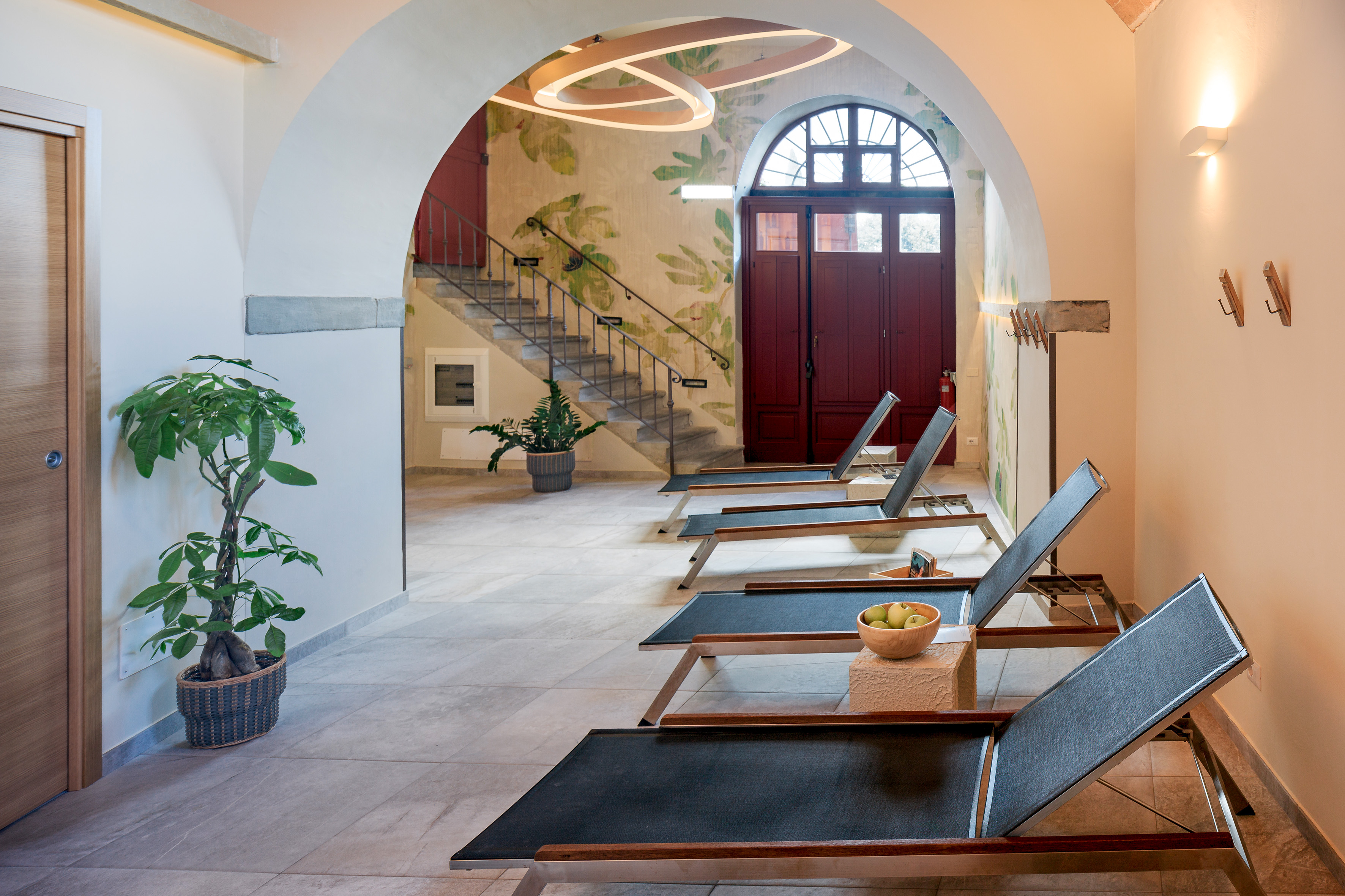 Spa relaxation area with modern lounge chairs, leaf mural, and arched interior.
