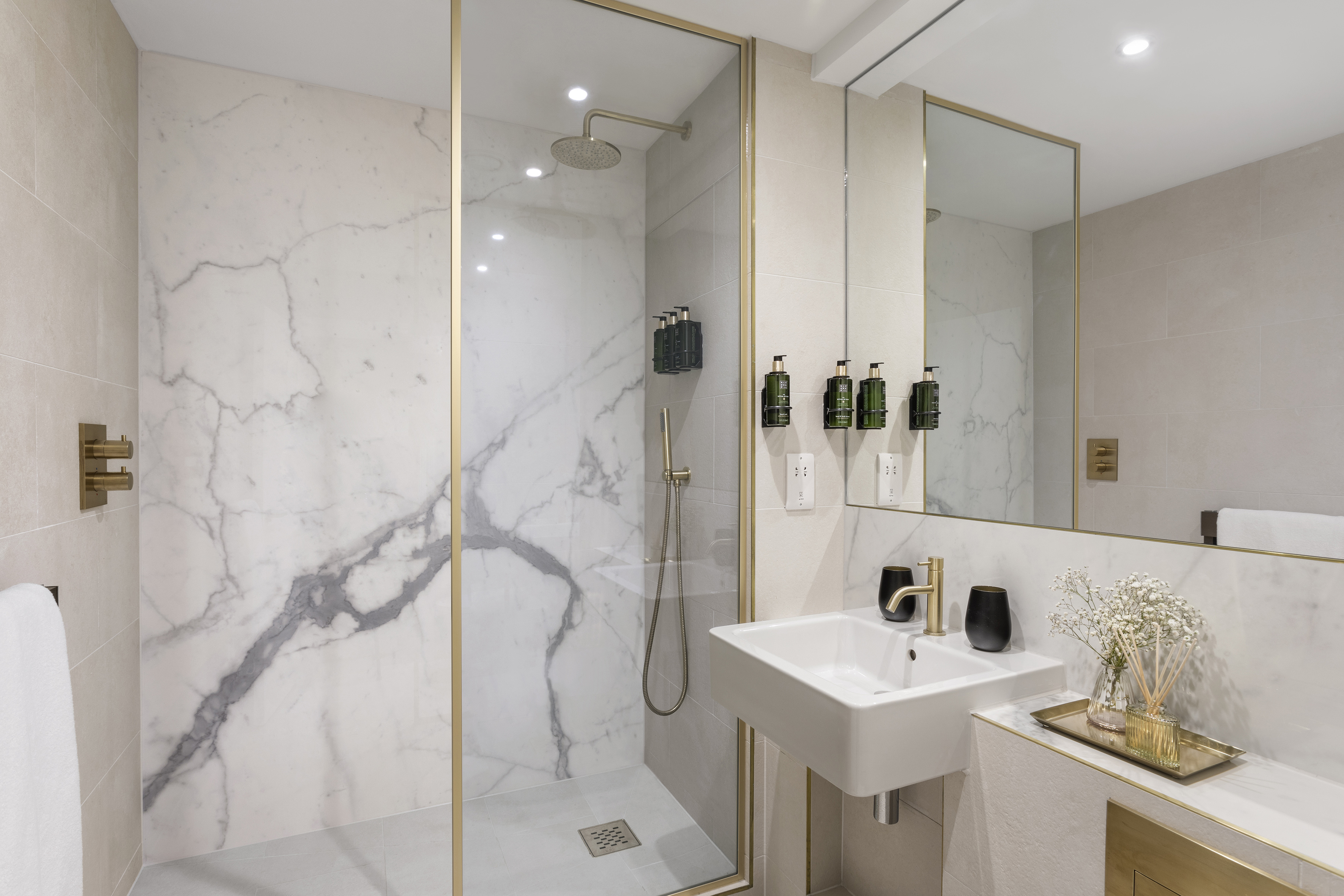 Contemporary bathroom with white marble walk-in shower and gold fixtures.
