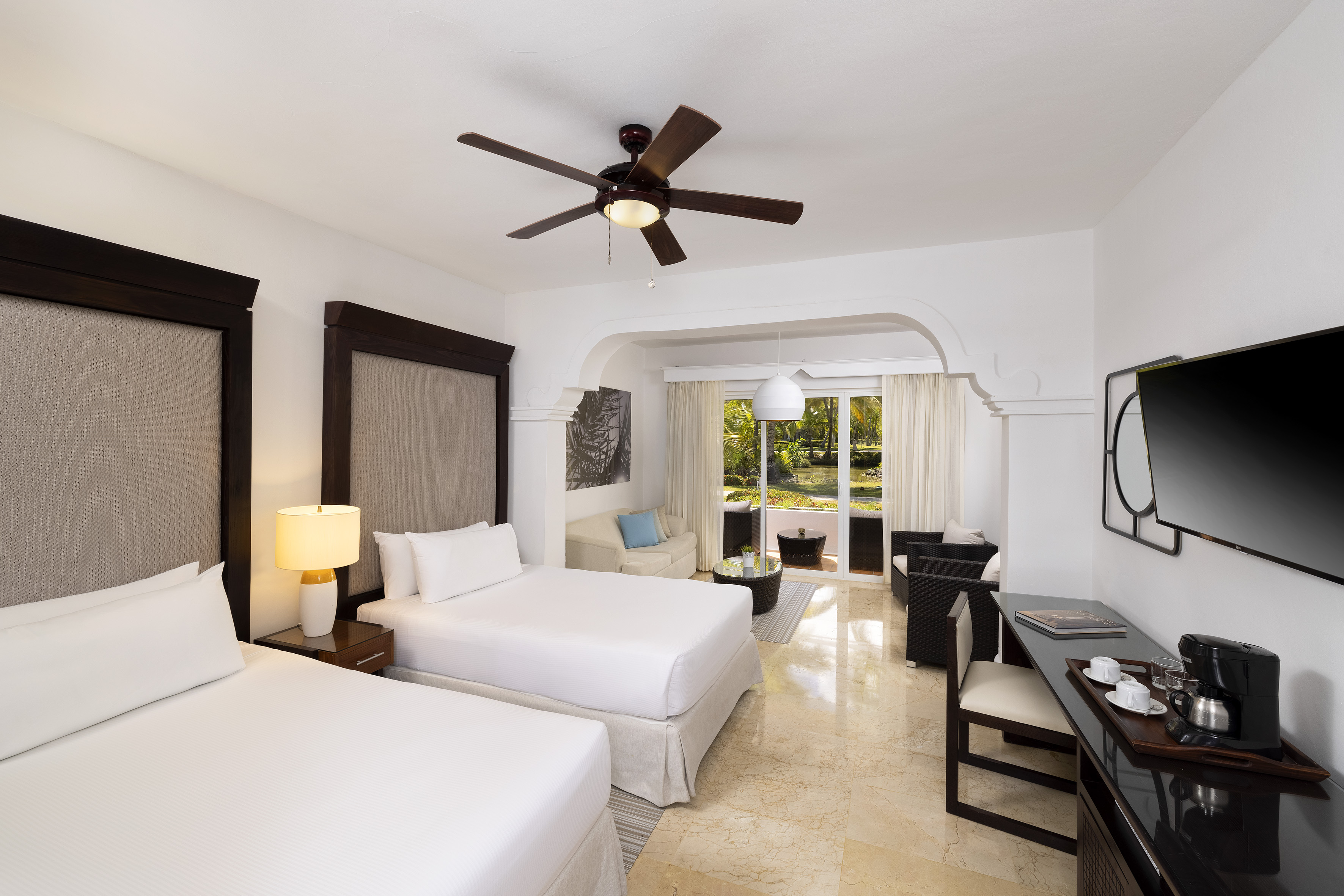 Spacious hotel suite with two beds, living area, and tropical garden view.