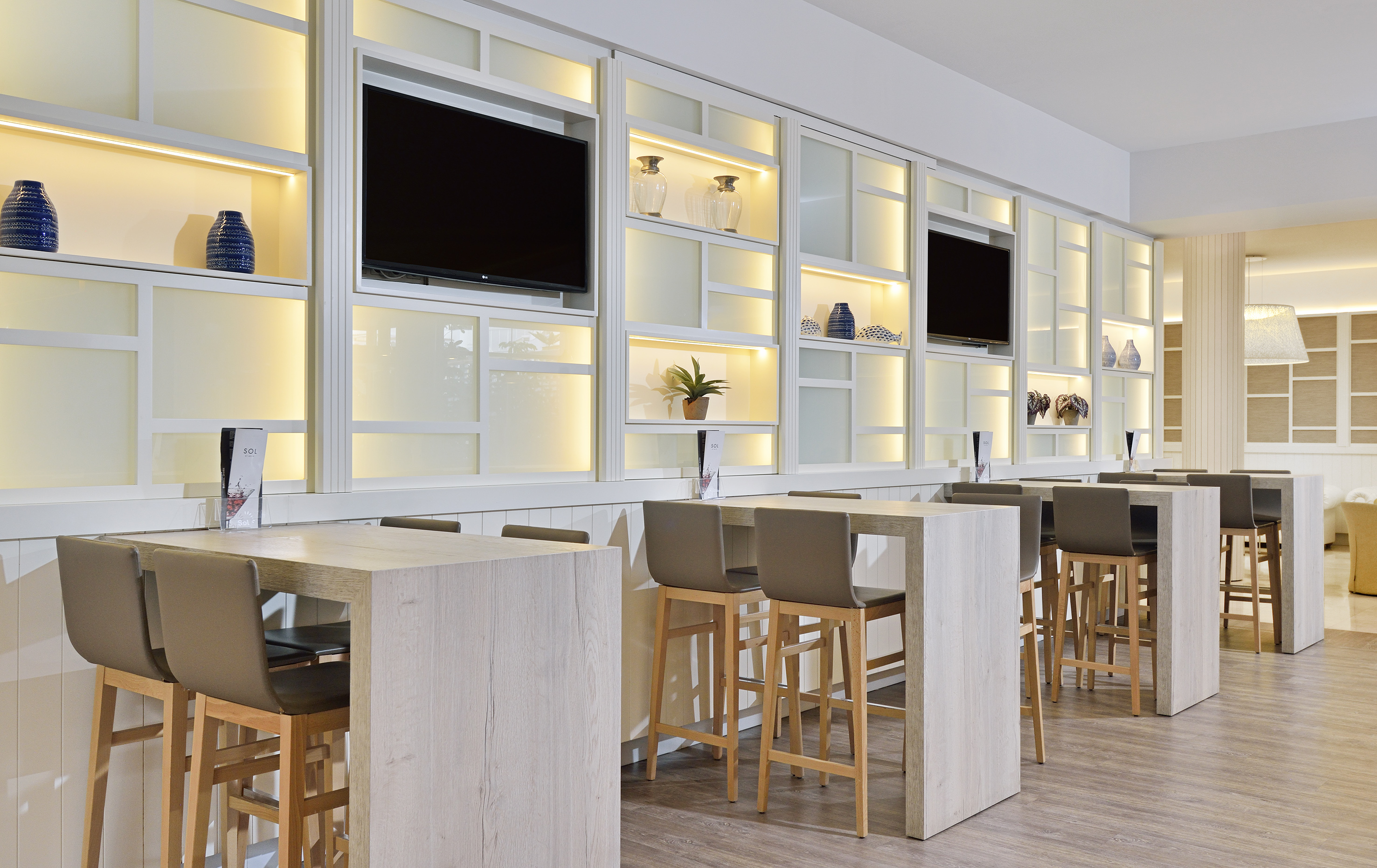 Modern bar area with high tables, stools, backlit shelving, and integrated TVs.