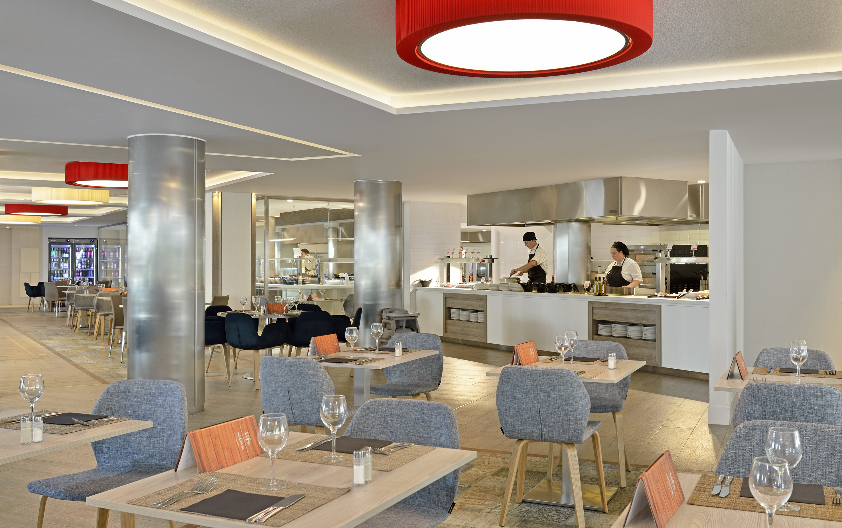 Hotel buffet restaurant with open kitchen, chefs, and contemporary dining tables.