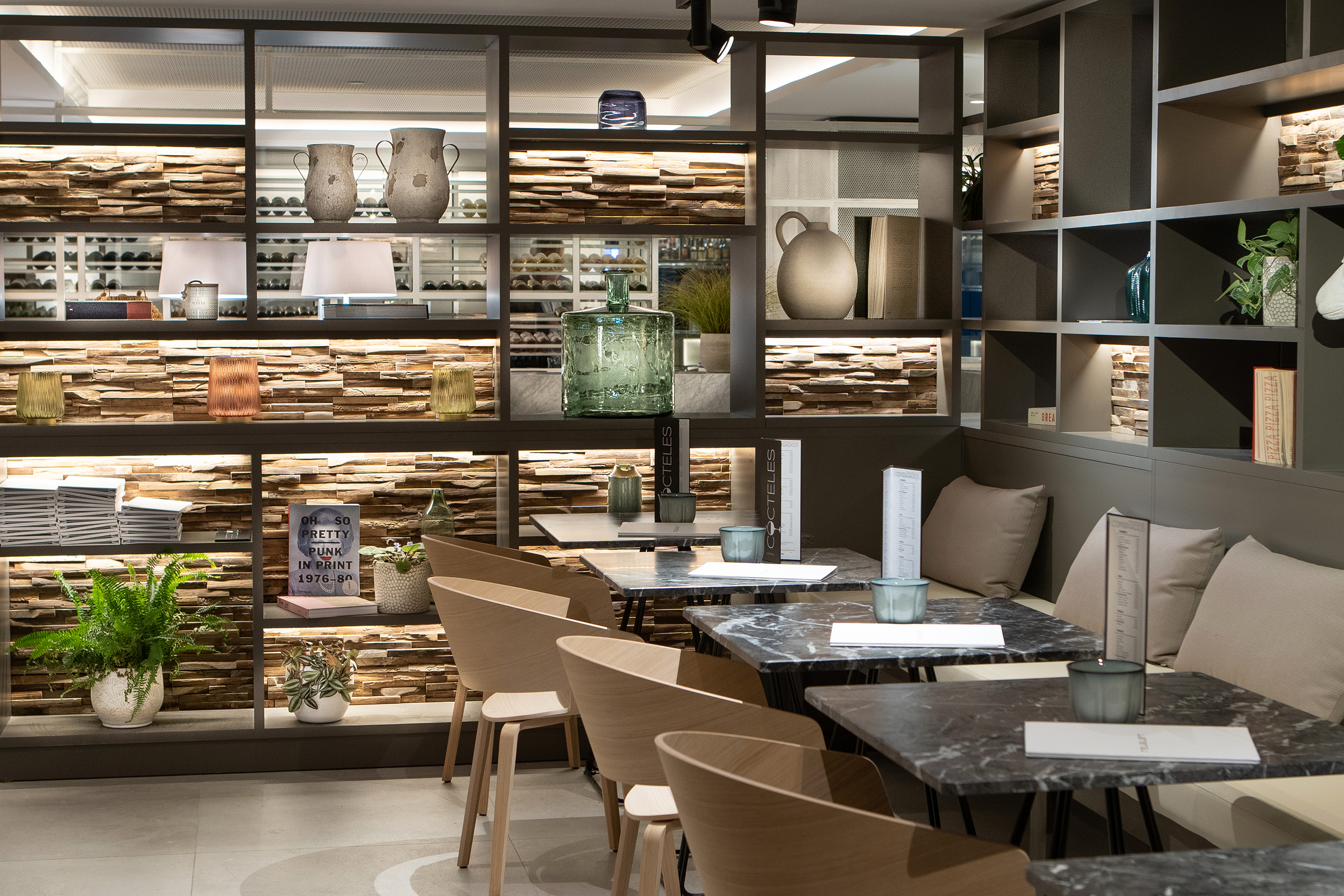 Modern restaurant interior with stylish decor, lighted shelves, and marble tables.