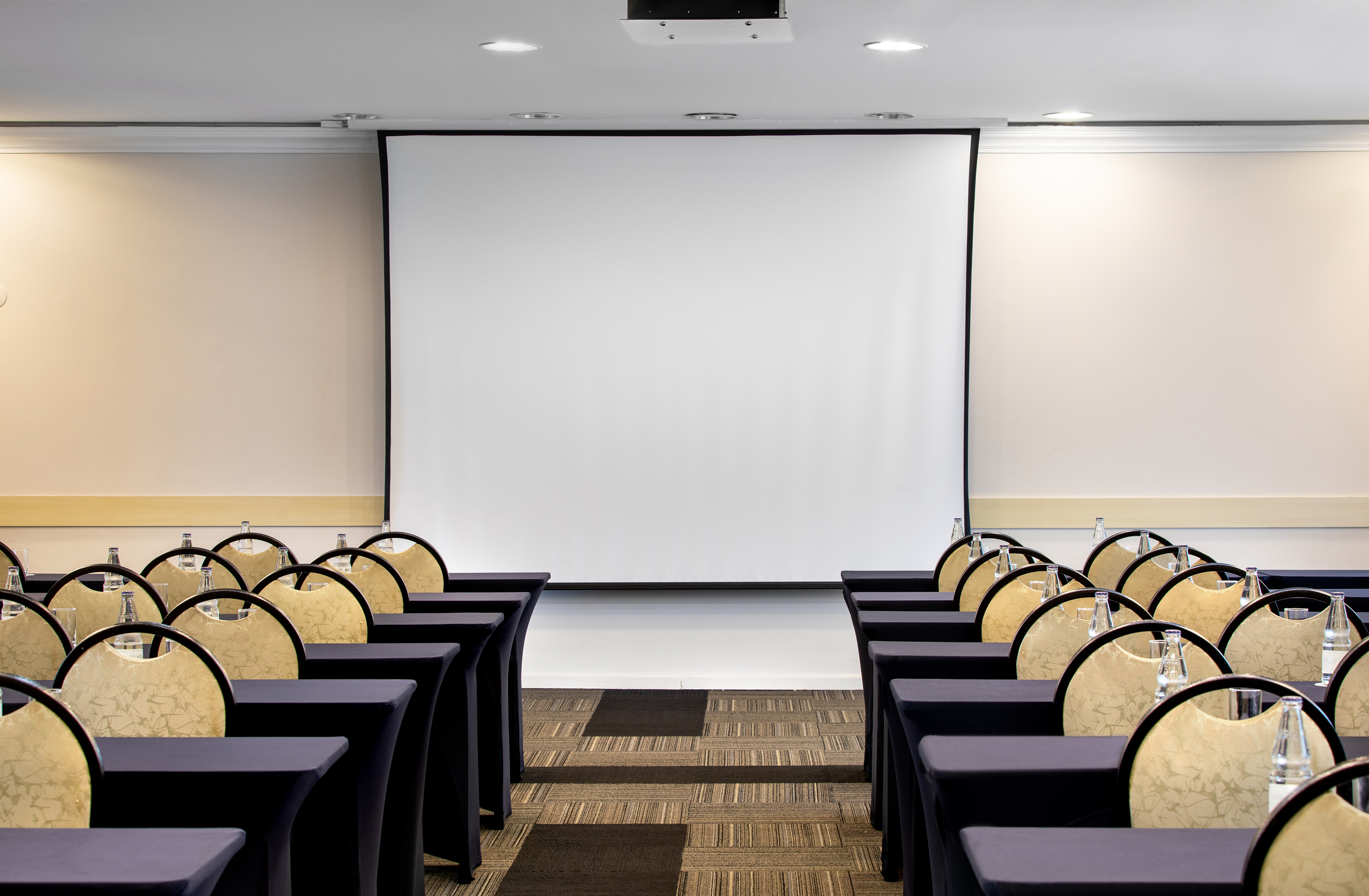 Conference room with tables, chairs, water, and projection screen.
