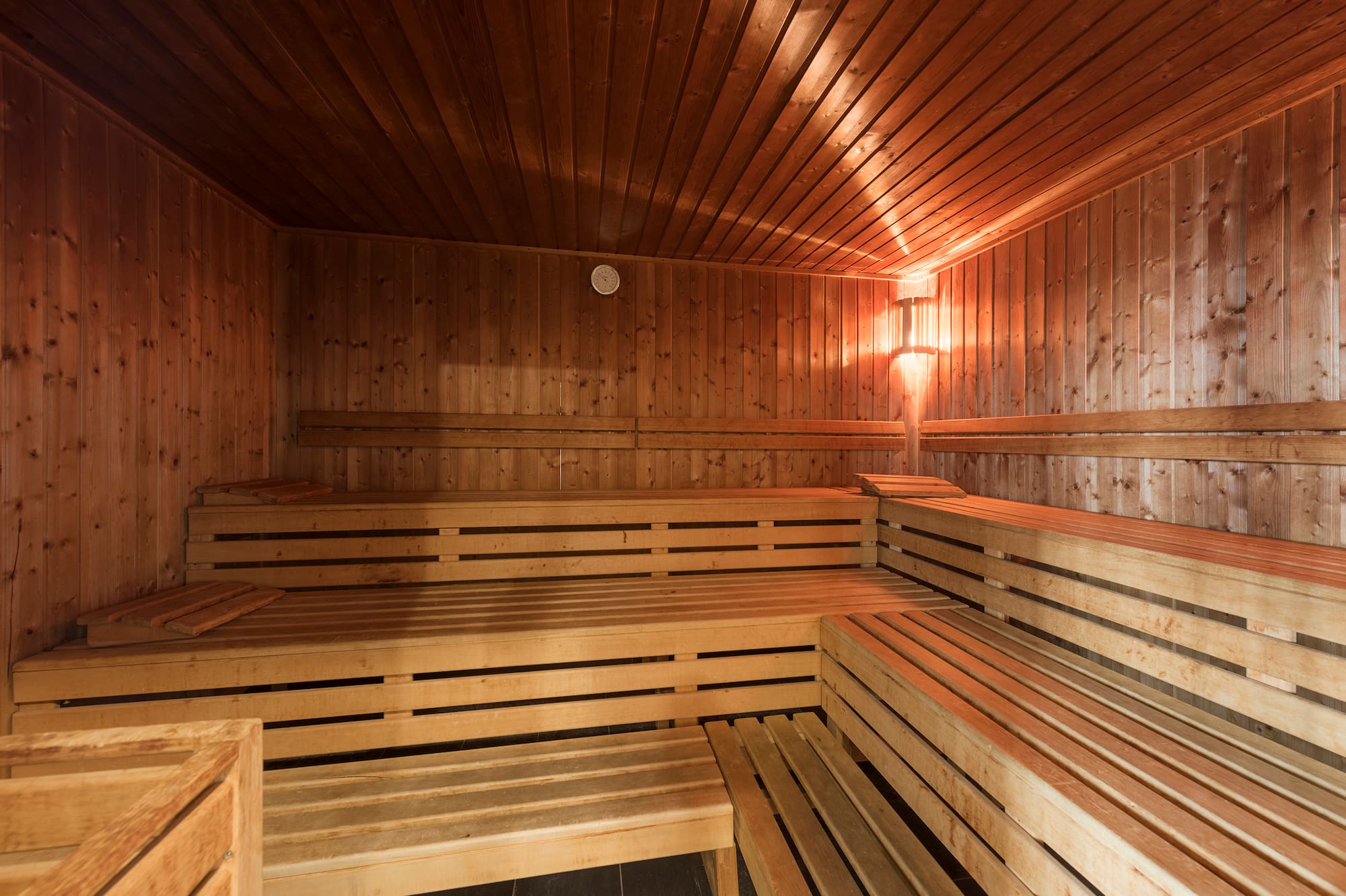 Wooden sauna with tiered benches, warm lighting, and a wall gauge.