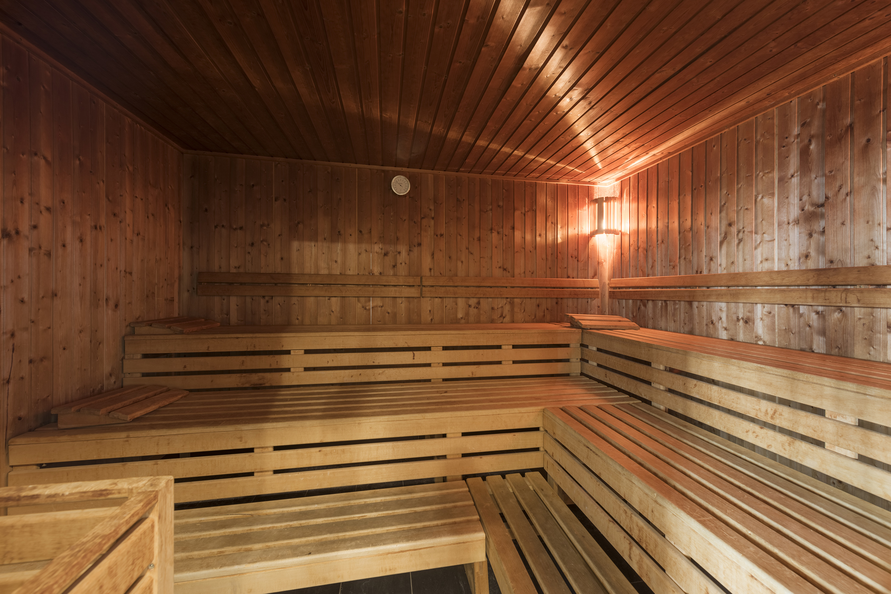 Wooden sauna with tiered benches, warm lighting, and a wall gauge.