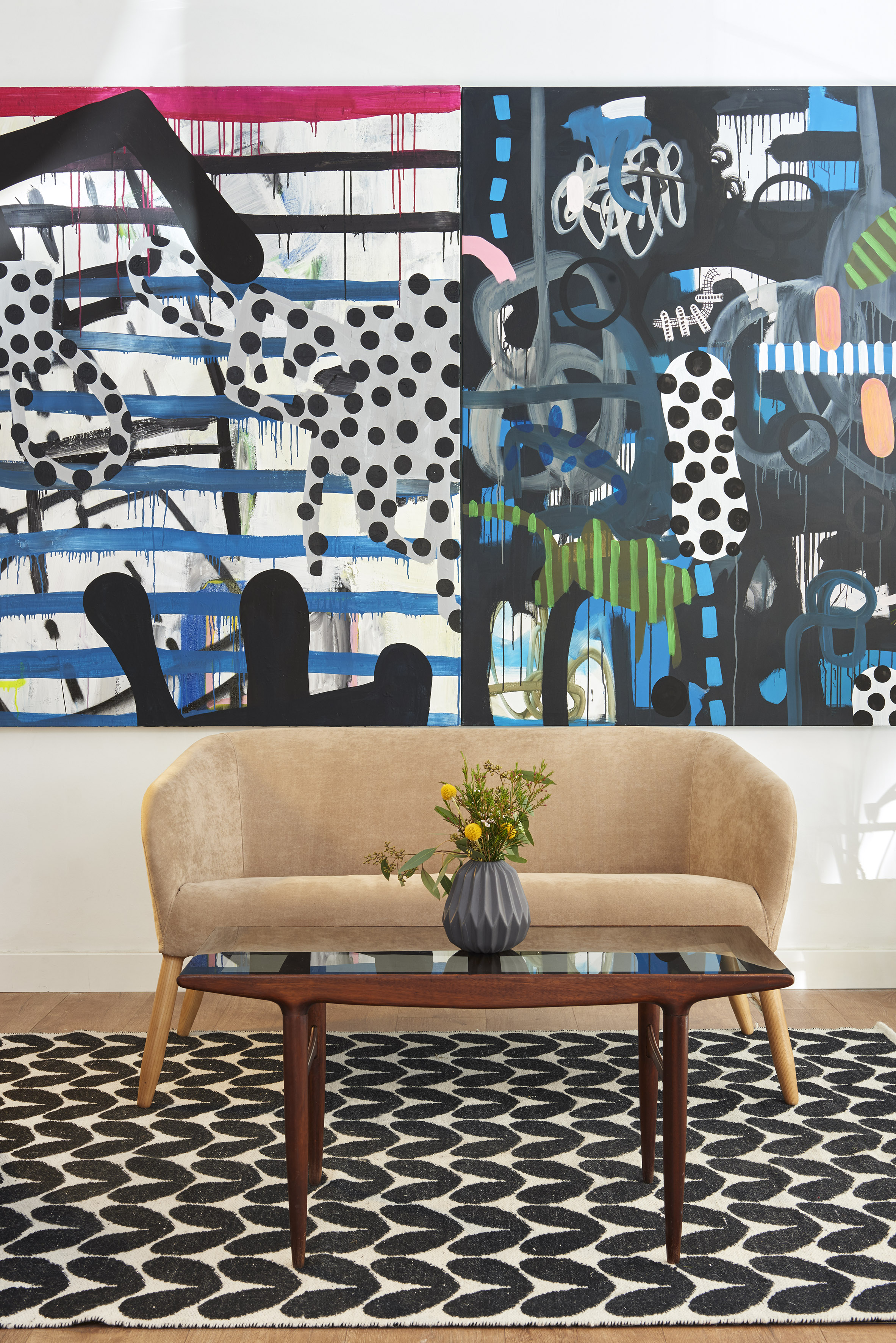 Modern living room with vibrant abstract art, beige sofa, wood coffee table, geometric rug.