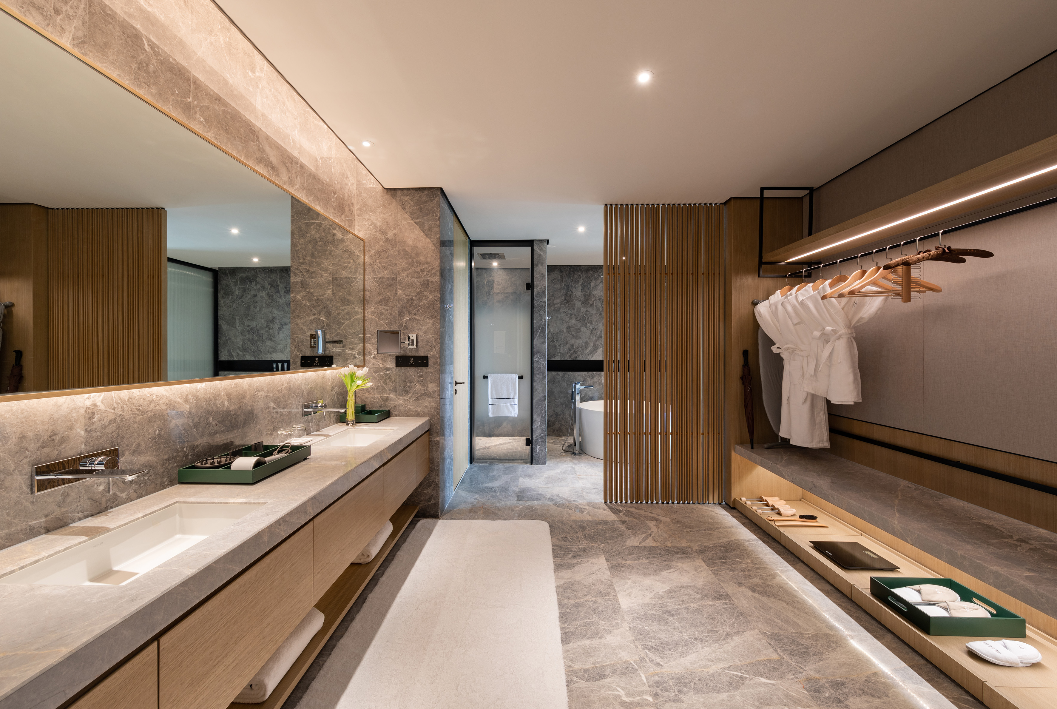 Modern luxury bathroom with marble double vanity, bathrobes, and walk-in shower.