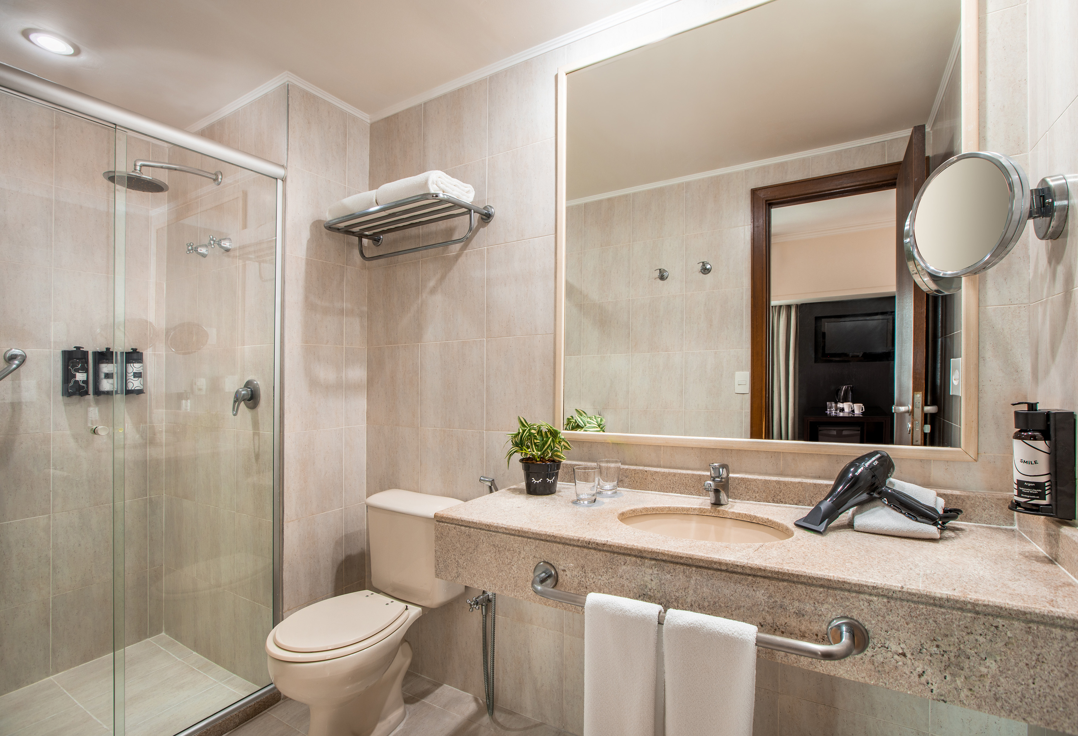 Tiled bathroom with glass shower, toilet, vanity, mirror, and hairdryer.