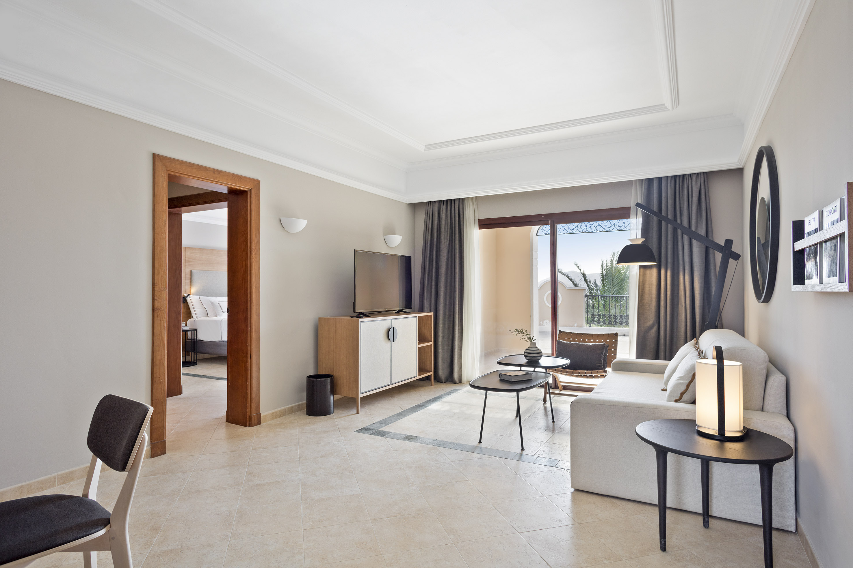 Bright modern hotel suite living room with balcony and connecting bedroom.