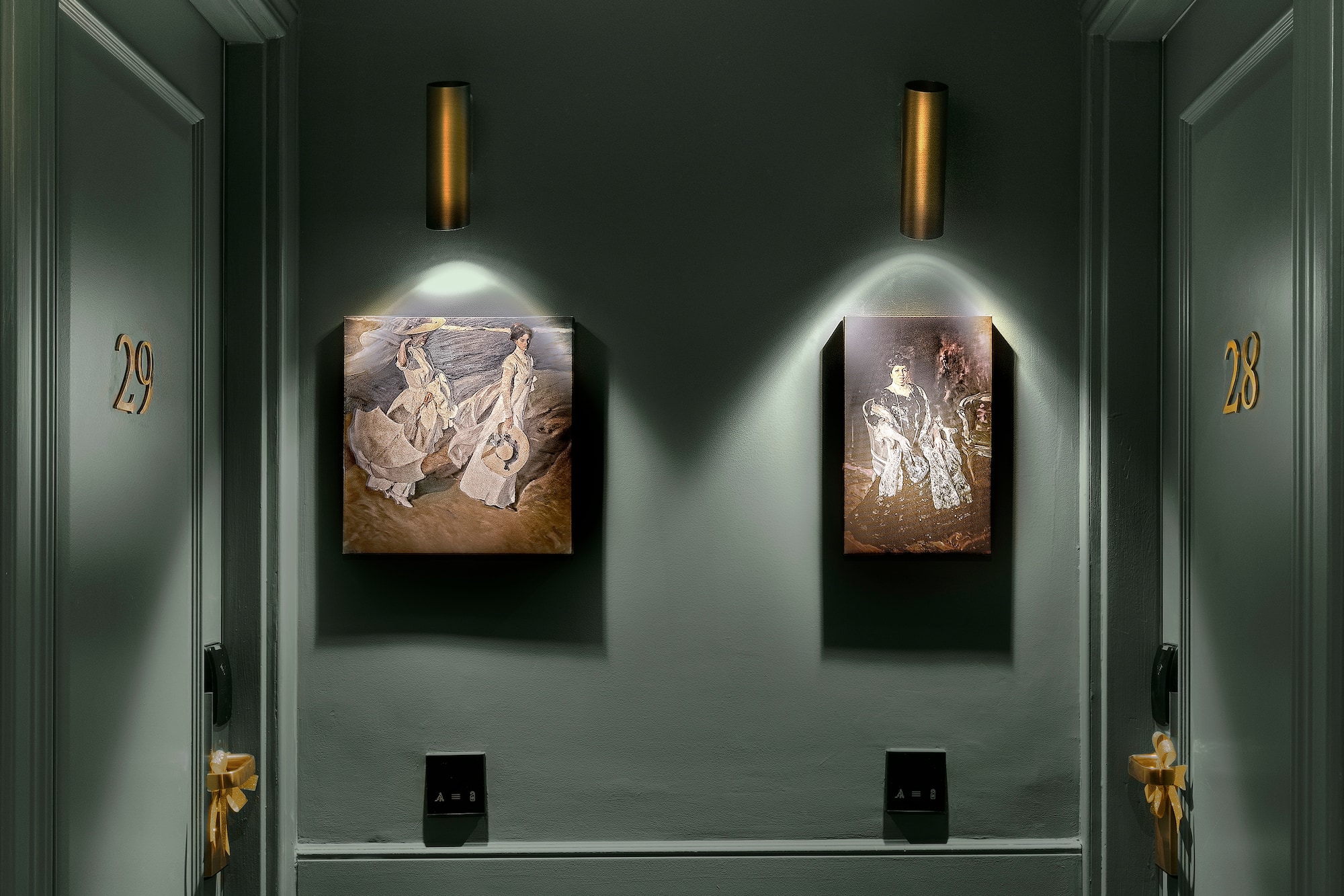 Dark hotel hallway with numbered room doors, elegant art, and brass wall sconces.