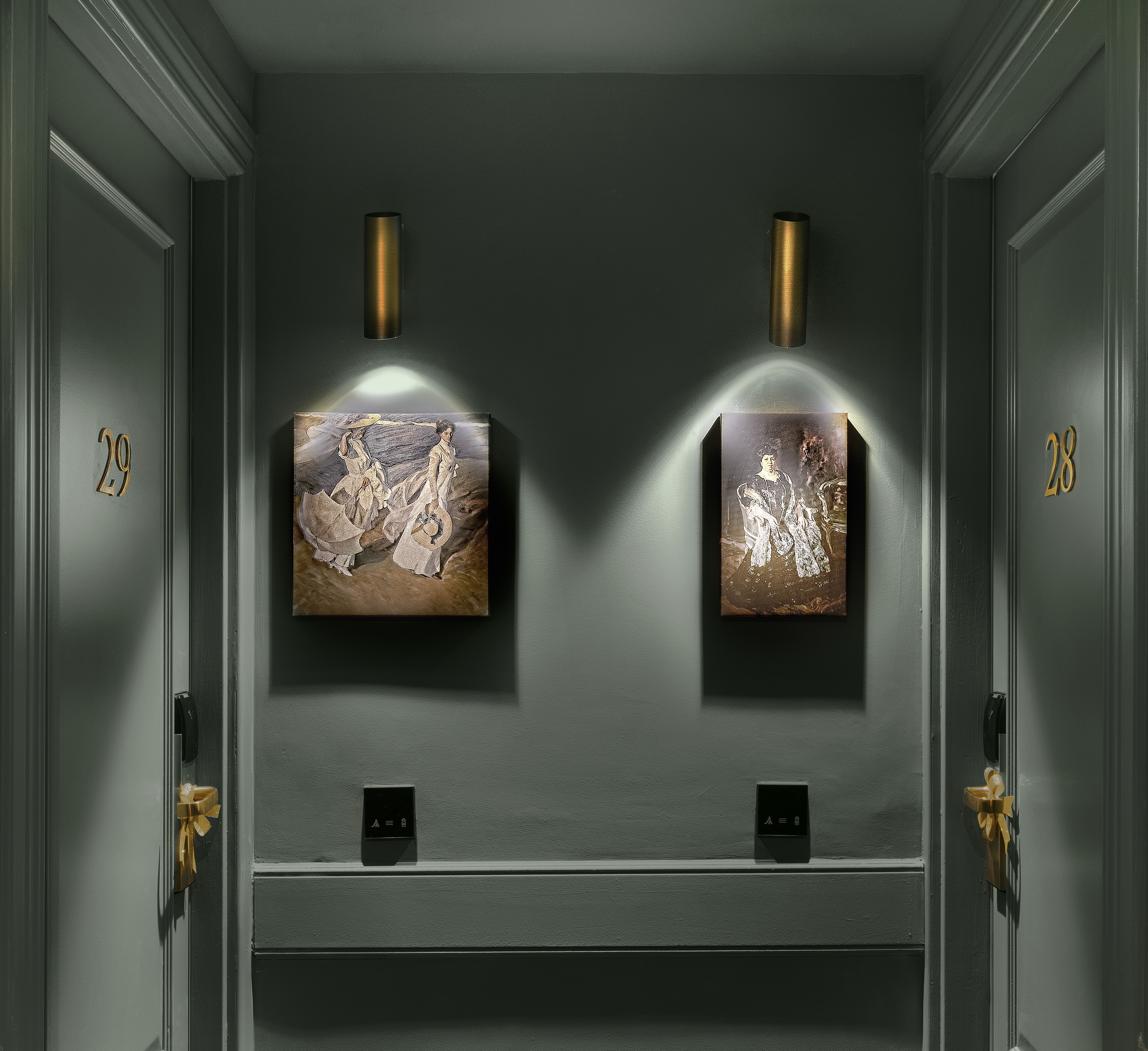 Dark hotel hallway with numbered room doors, elegant art, and brass wall sconces.