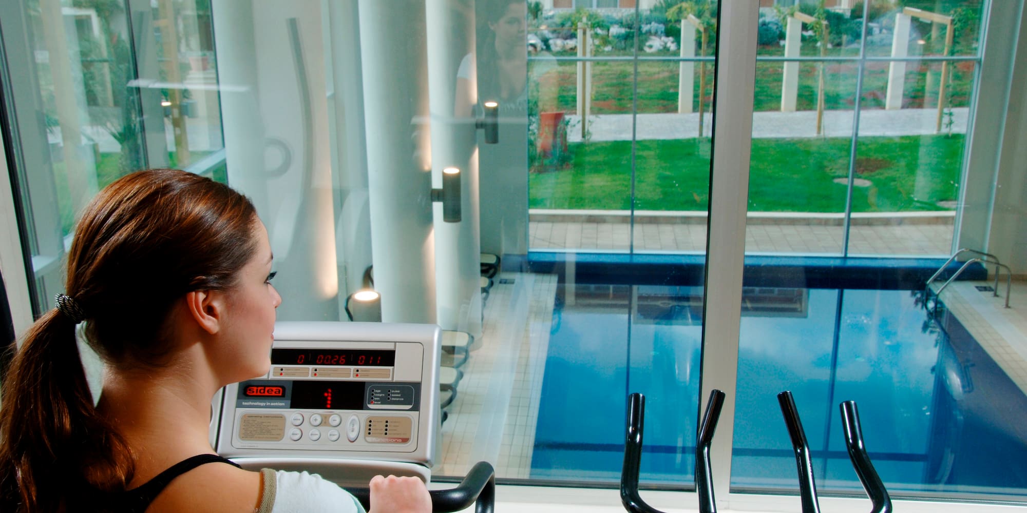 a woman on a treadmill looking at a pool