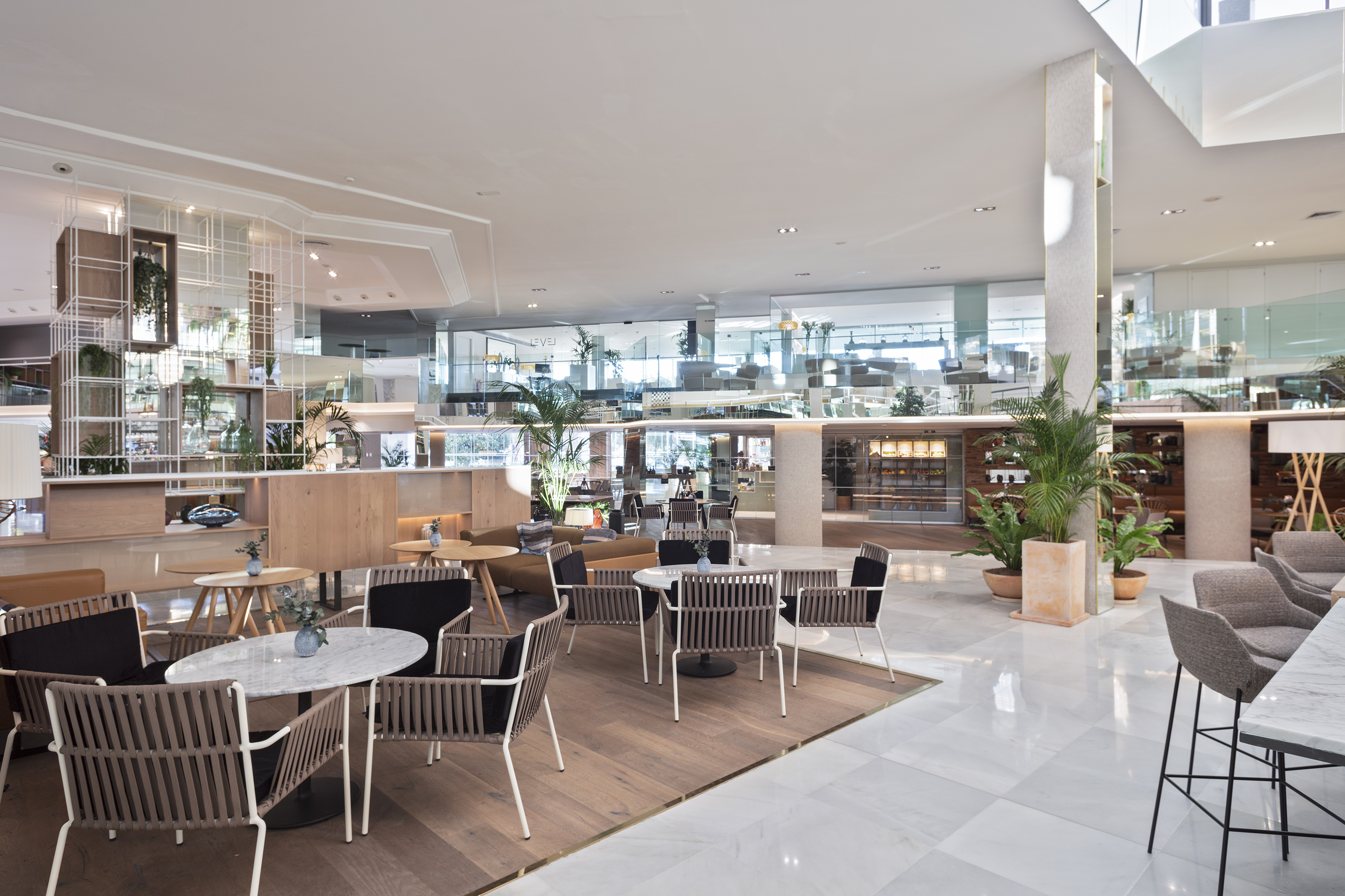 Modern hotel lounge with cafe seating, marble floors, and potted plants.