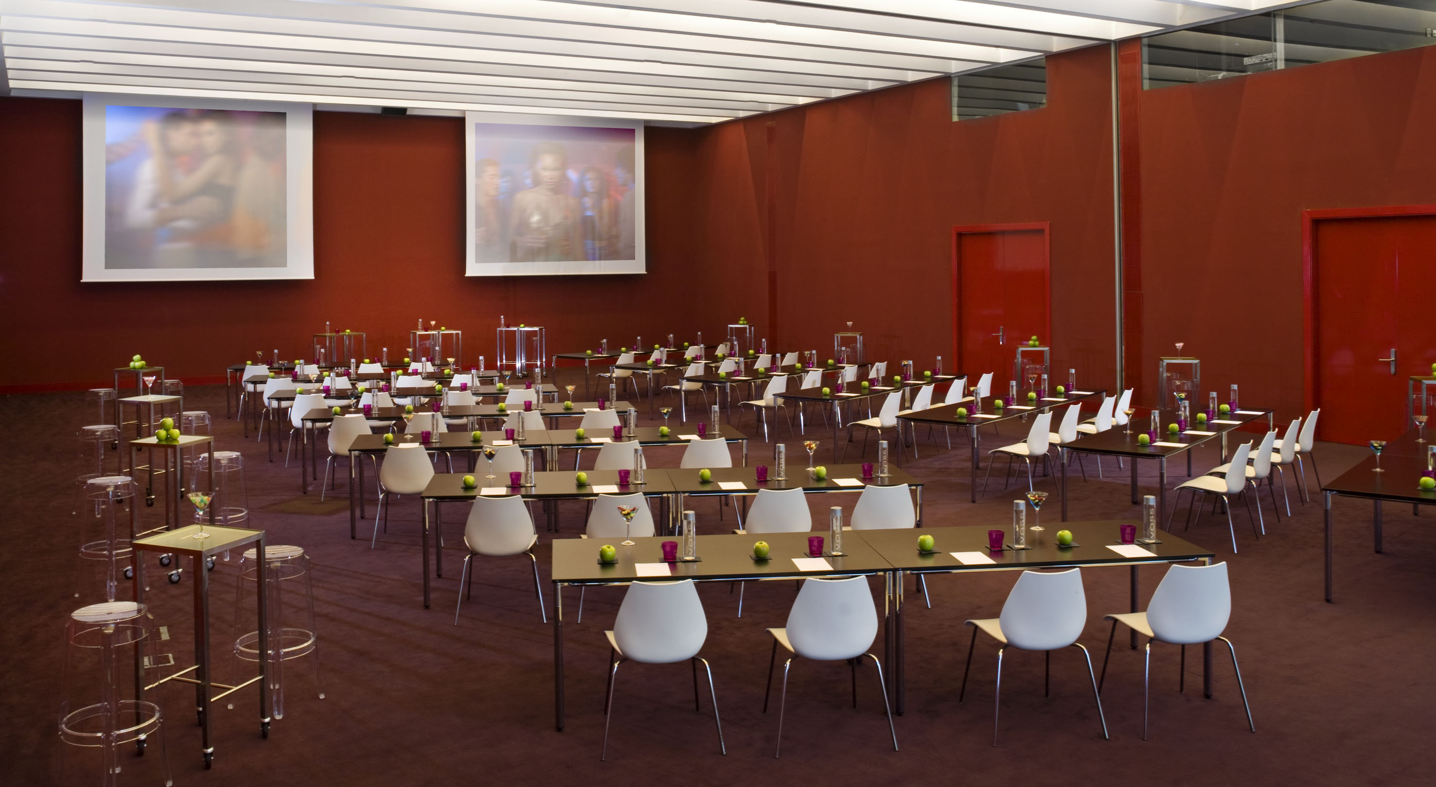 Modern event space with rows of tables, white chairs, and dual projection screens.