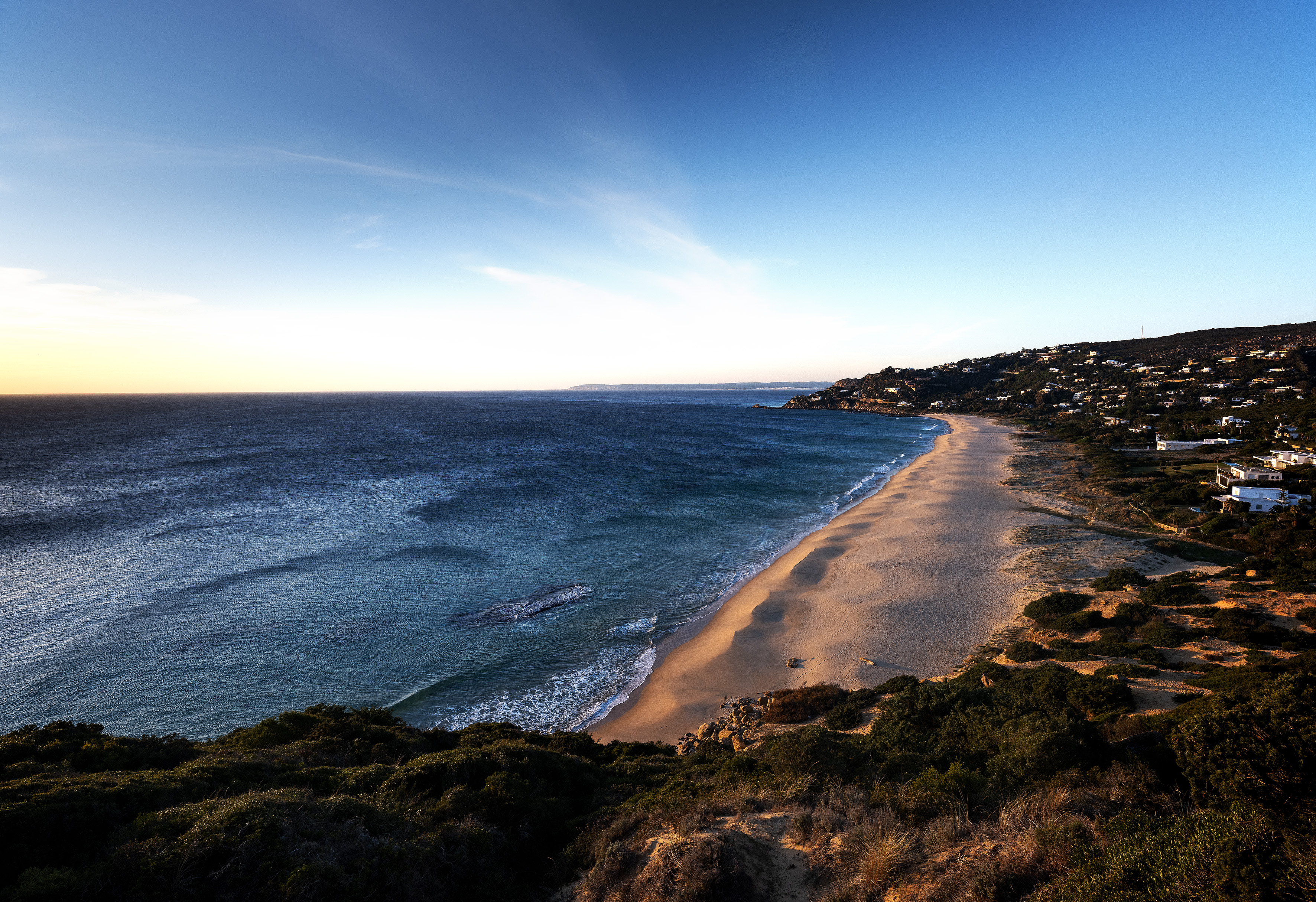 Sandy beach, blue ocean waves, and coastal hillside homes.