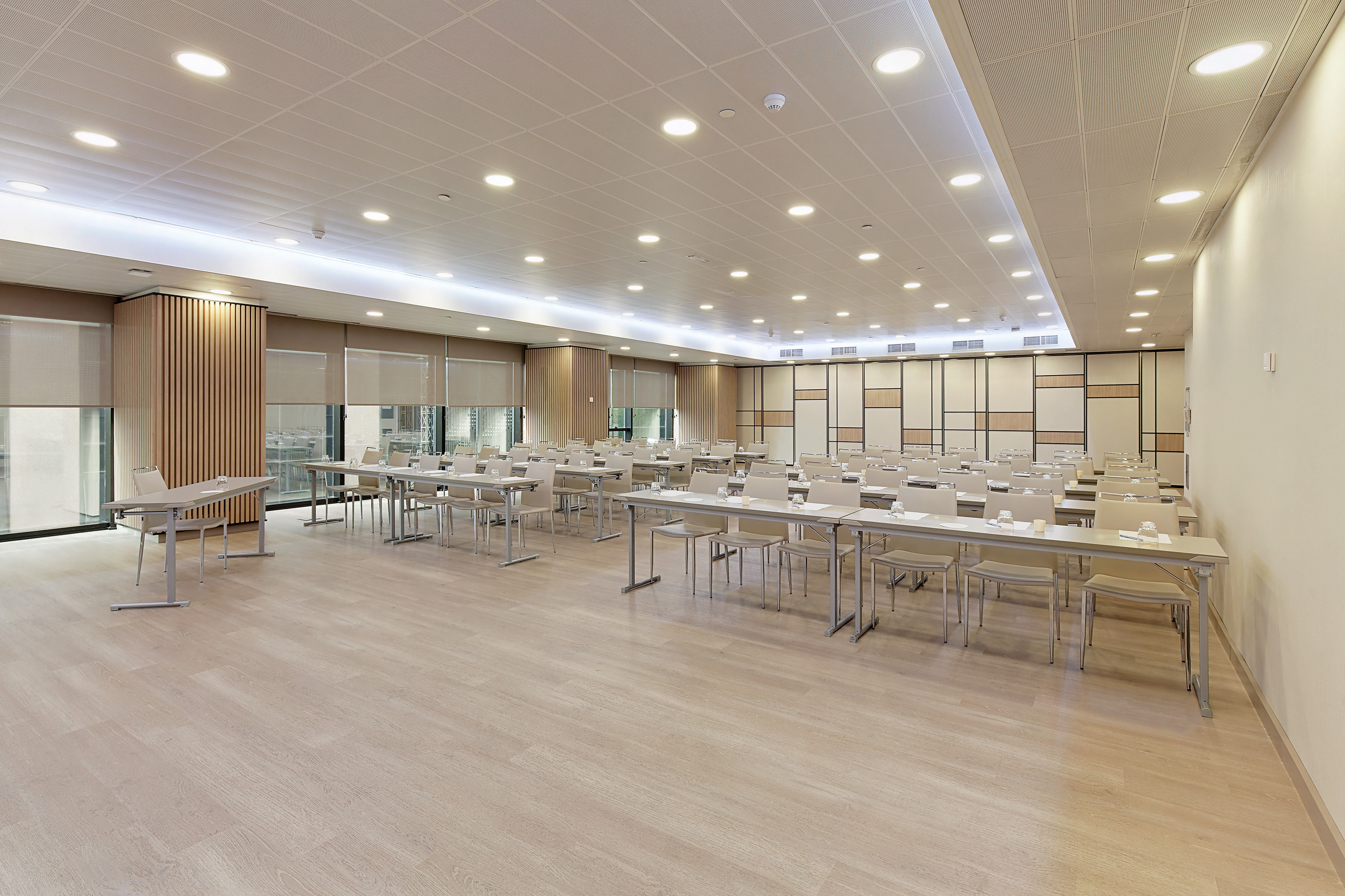 Bright, modern conference room with empty tables and chairs, light wood floor.