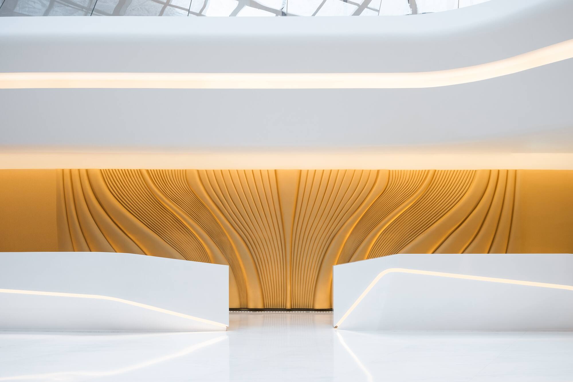 Contemporary reception lobby with white desks and backlit golden textured wall.