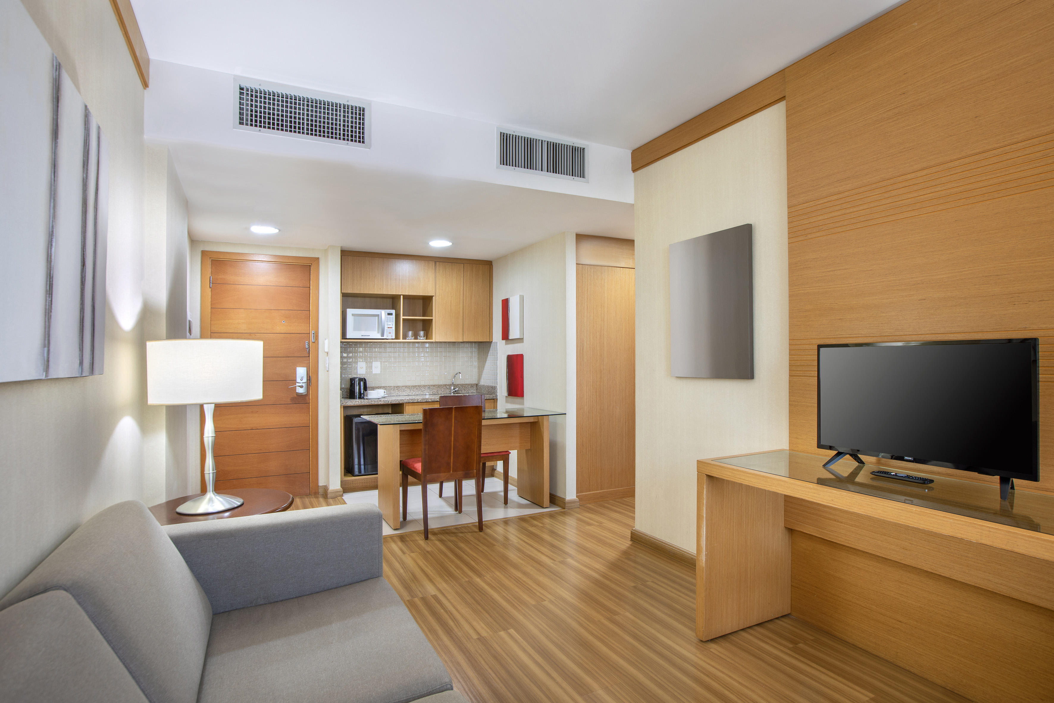 Modern hotel studio apartment with kitchenette, sofa, dining table, and TV.