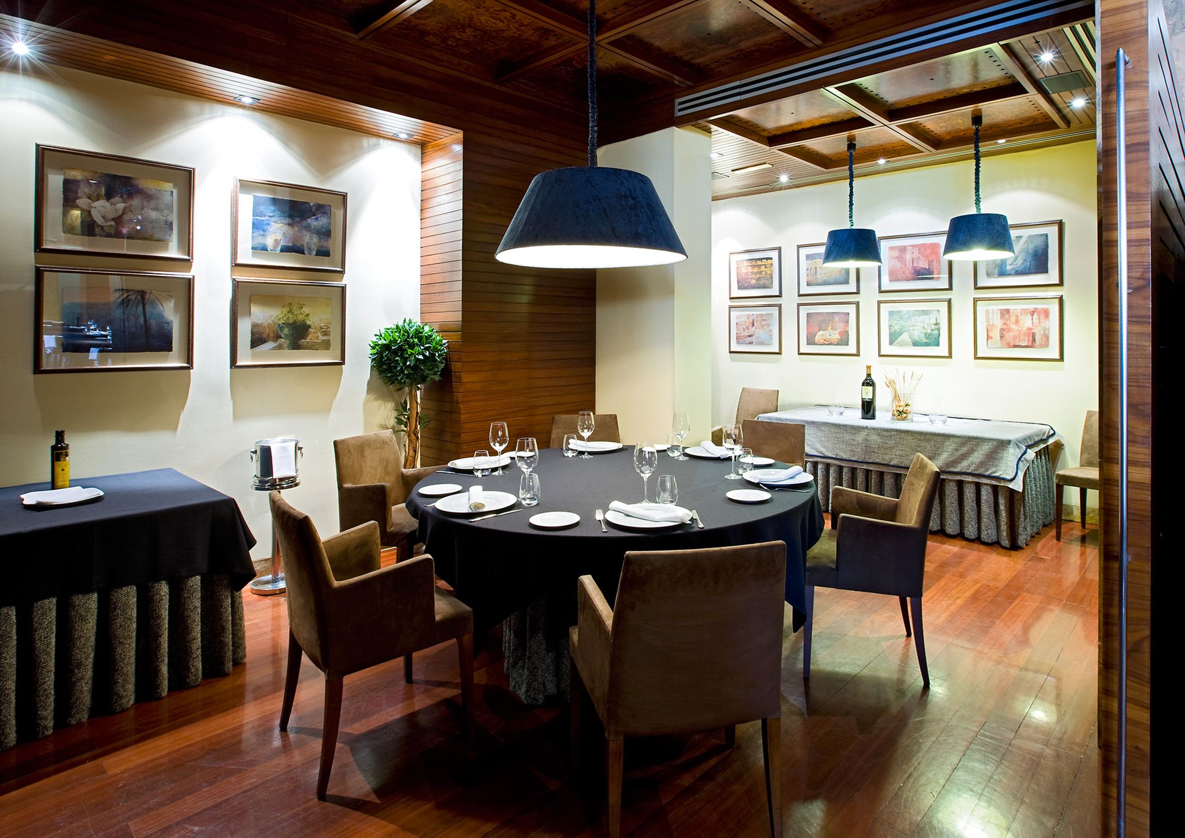 Restaurant dining room with round table, brown chairs, and framed art.